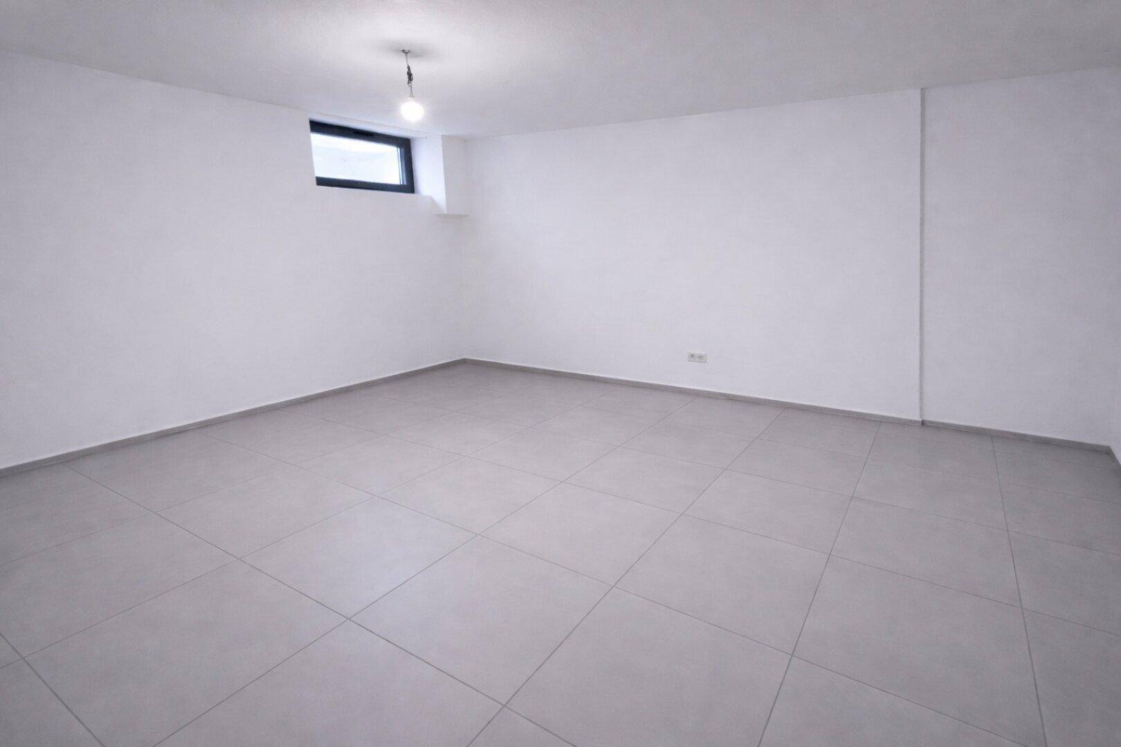 Heller Kellerraum mit Fliesenboden und einem kleinen Fenster, ideal als Hobbyraum.