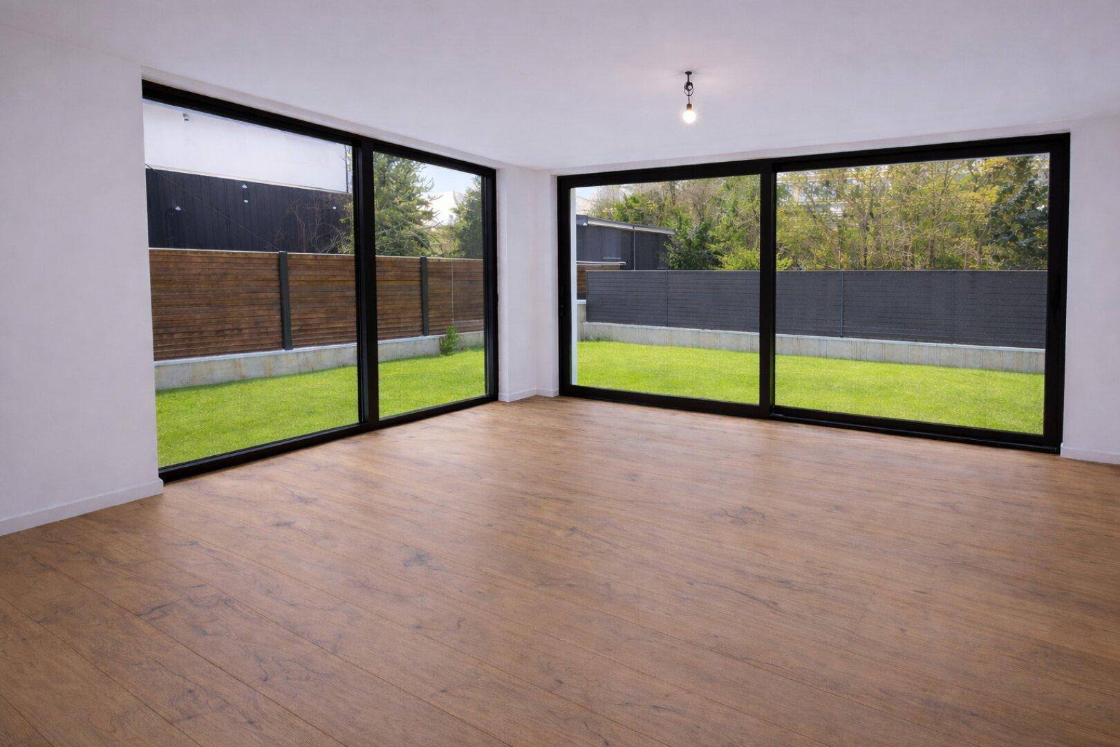 Heller Wohnbereich mit großen Fenstern, Holzboden und Blick ins Grüne.