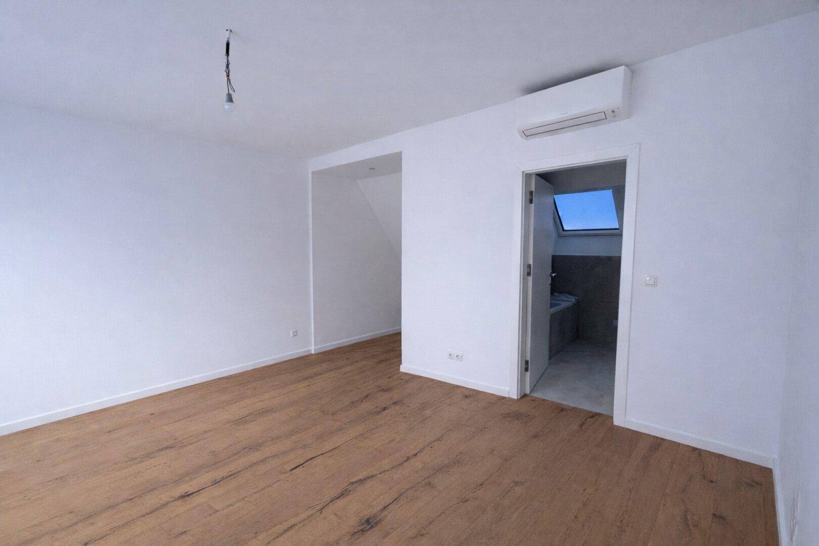 Helles Zimmer mit Holzboden, Klimaanlage und Zugang zu einem Badezimmer.