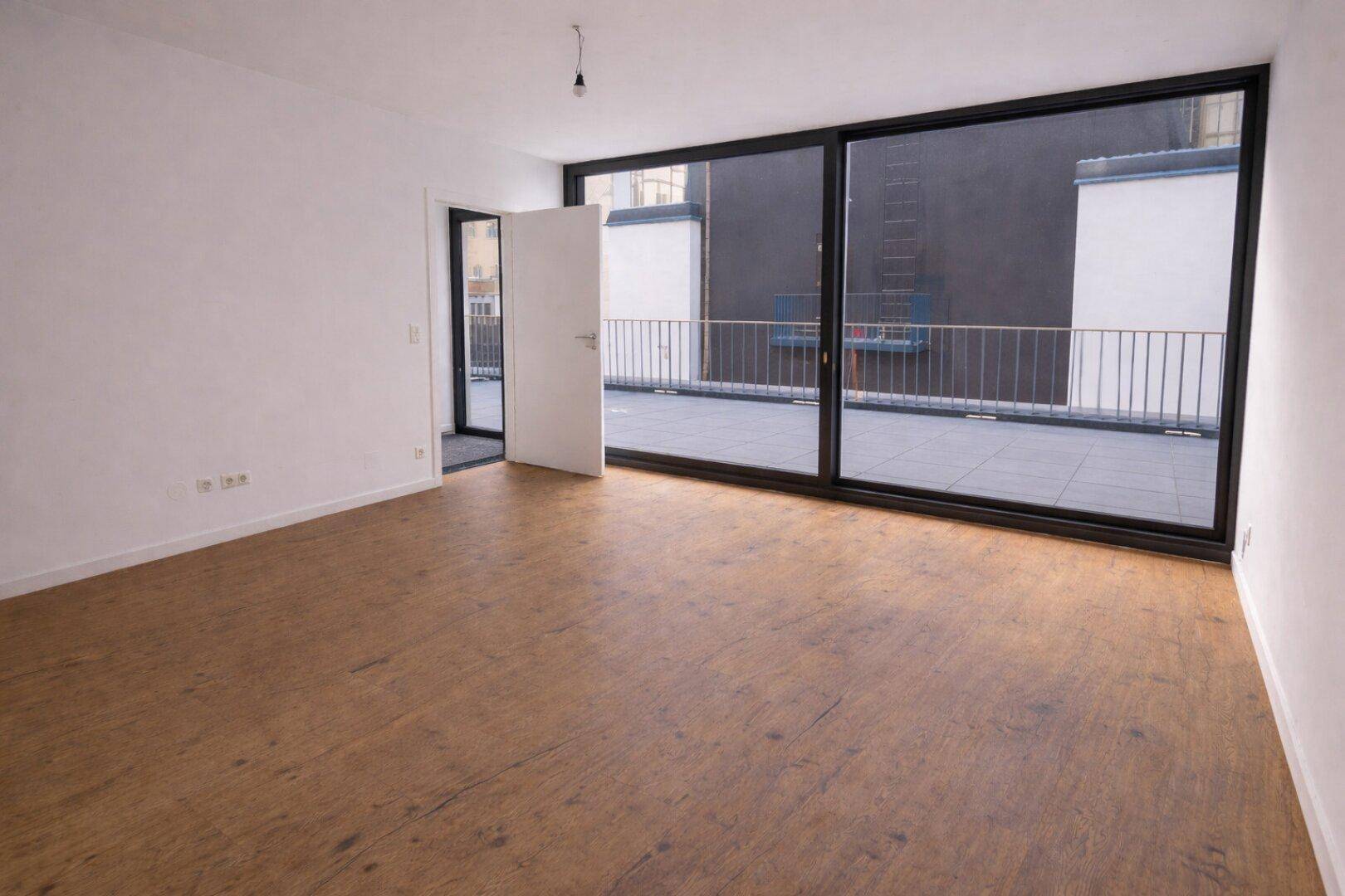 Großzügiger Raum mit Holzboden und breiter Schiebetür zur Terrasse.