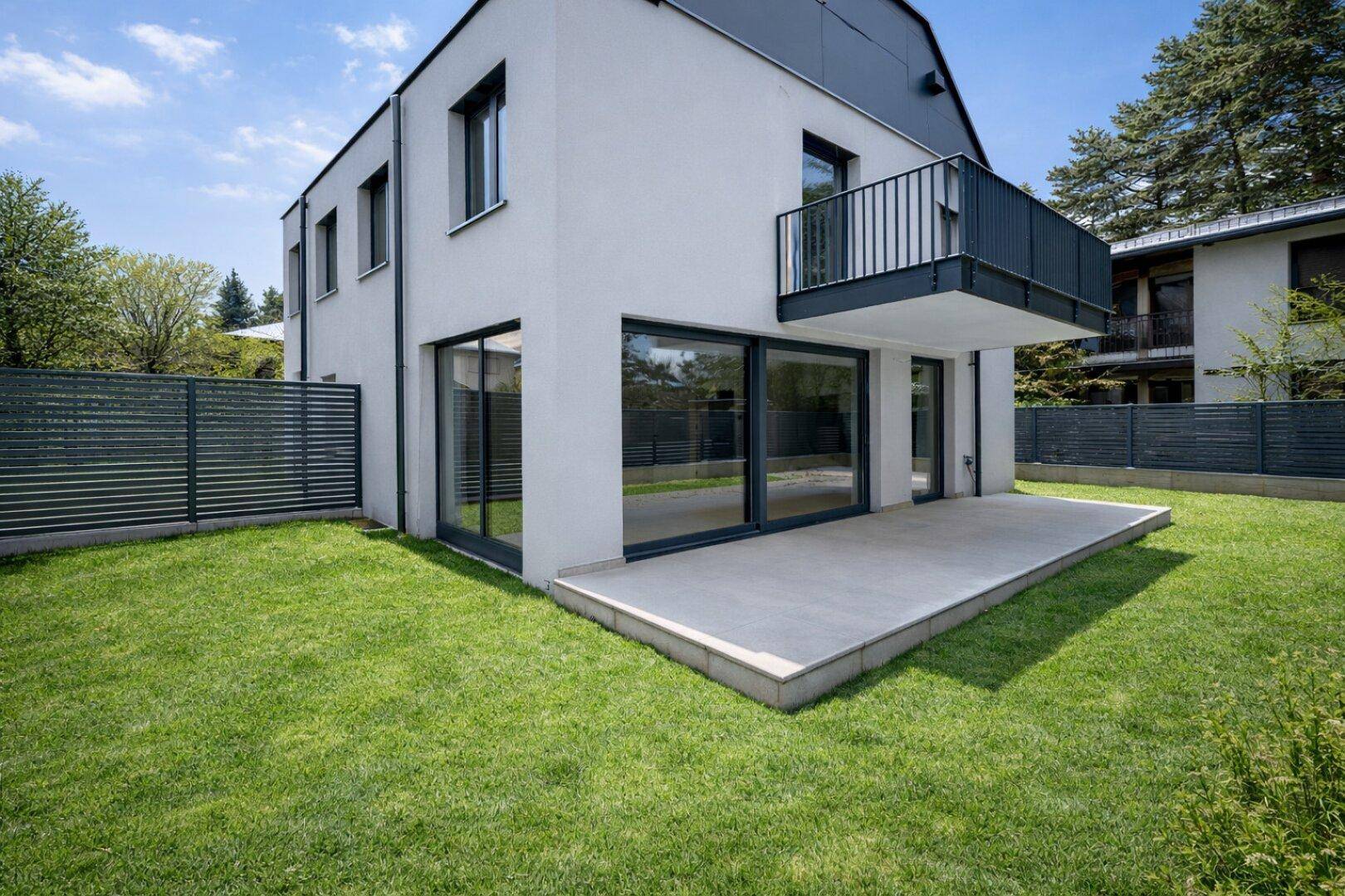 Moderne Hausfassade mit großer Terrasse und Rasenfläche im Gartenbereich.