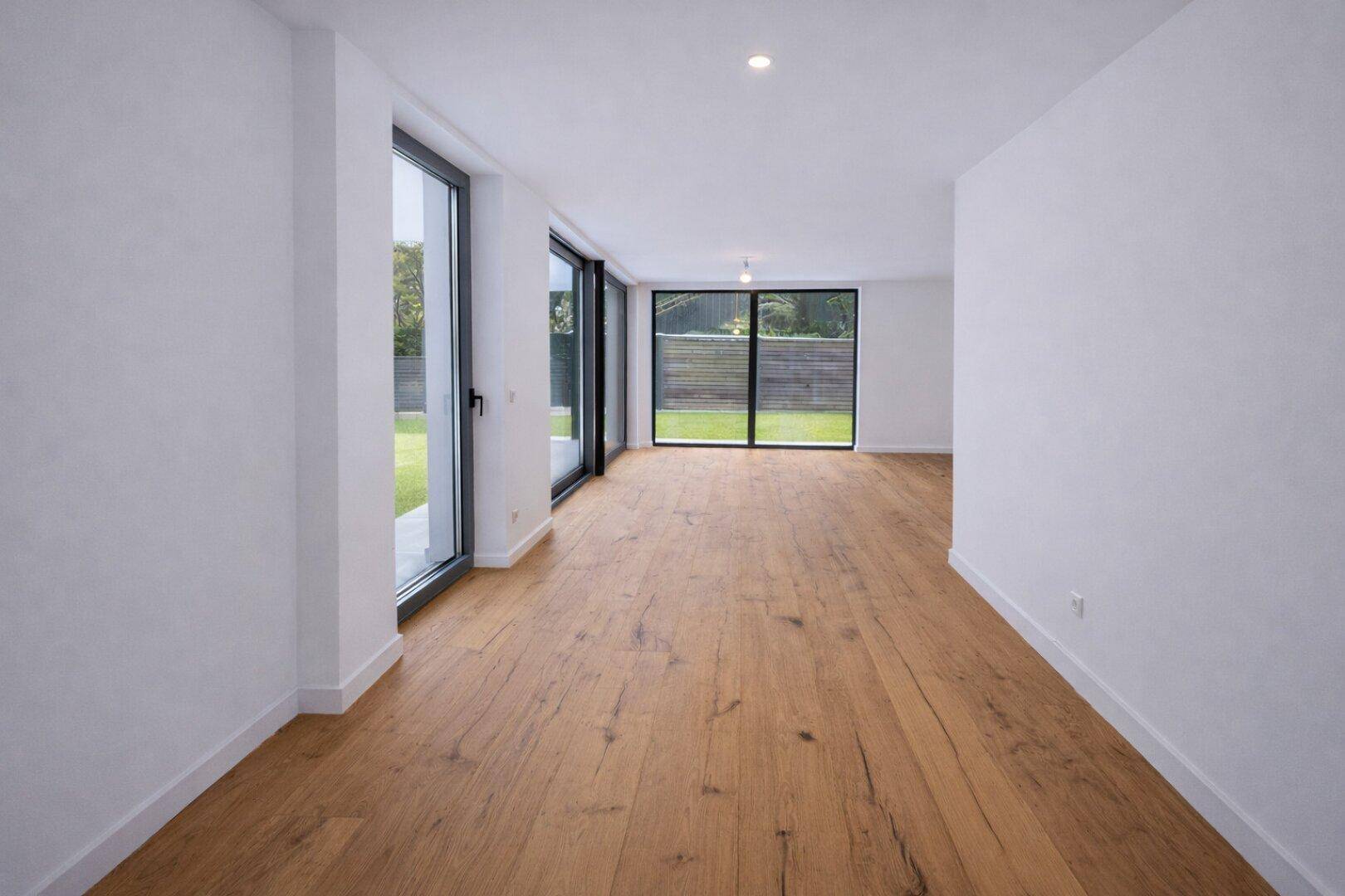 Geräumiger, heller Raum mit Holzboden und mehreren bodentiefen Fenstern zum Garten.