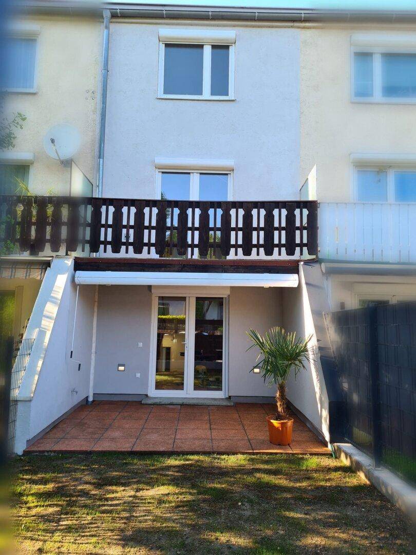Rückansicht eines Reihenhauses mit Terrasse, kleinem Garten und einem Balkon im Obergeschoss.
