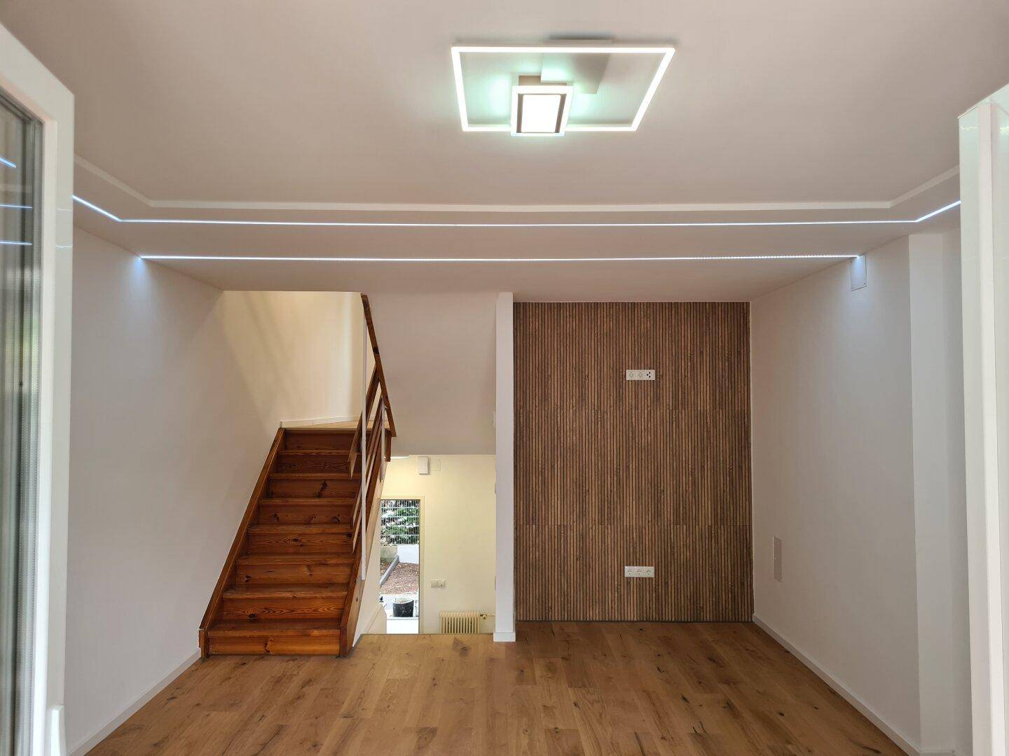 Heller Wohnbereich mit modernem Deckenlicht, Holzfußboden und einer stilvollen Holzlamellenwand.