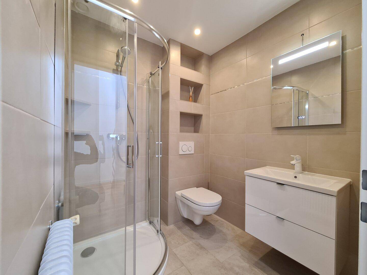 Modernes Badezimmer mit beigefarbenen Fliesen, eleganter Duschkabine und wandhängendem WC.