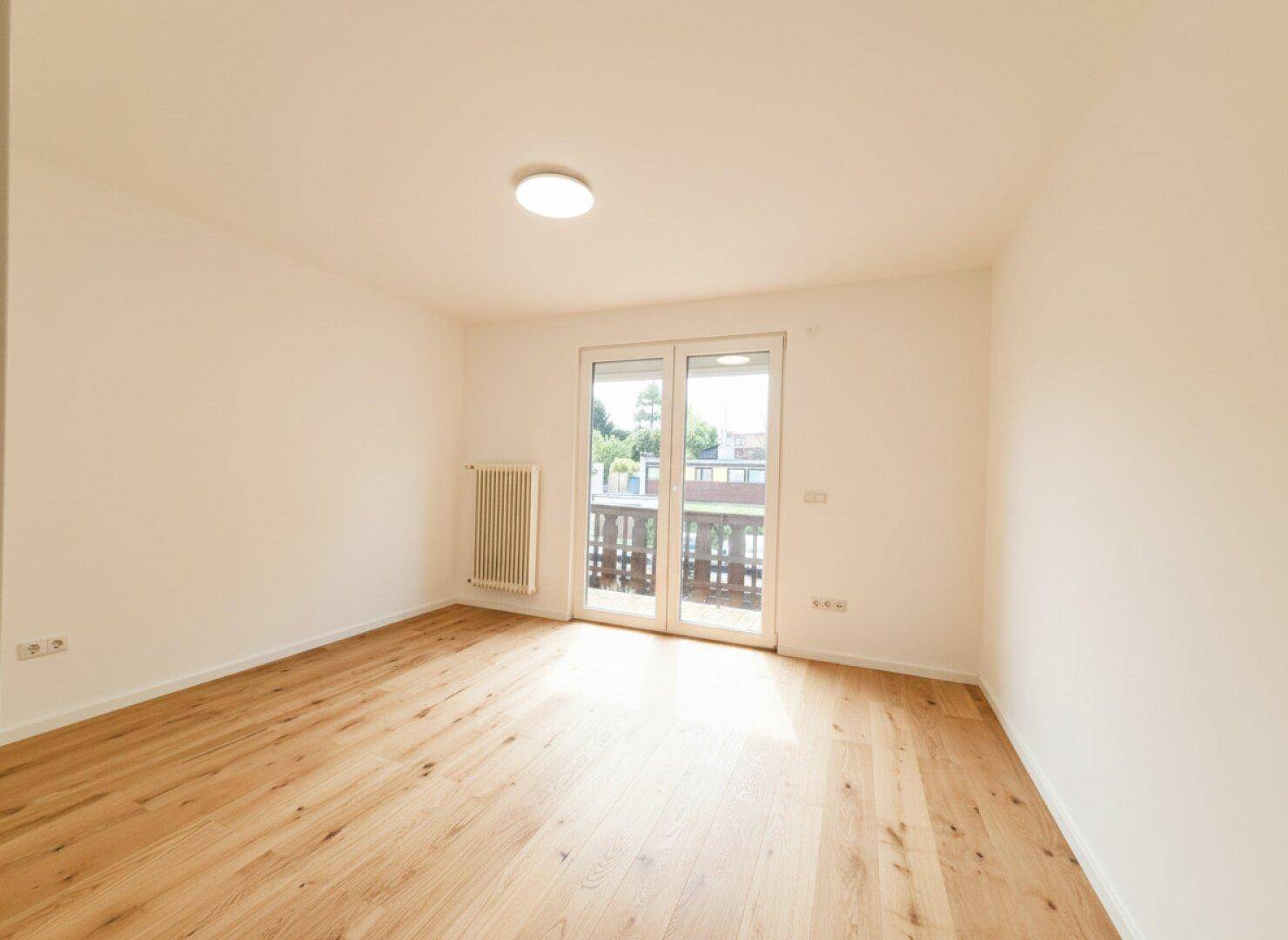 Helles Zimmer mit Holzfußboden und direktem Zugang zu einem Balkon, ideal als Schlaf- oder Arbeitszimmer.