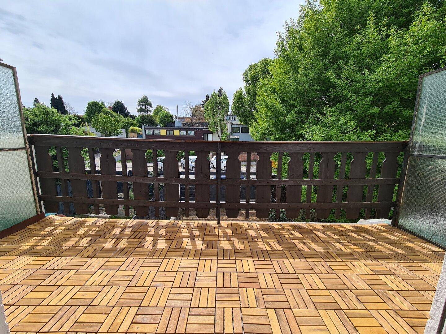 Geräumiger Balkon mit Holzbodenfliesen und Blick ins Grüne, perfekt für entspannte Stunden im Freien.
