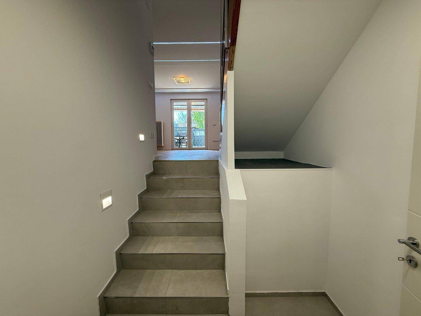 Moderne Treppe mit Fliesenstufen und integrierter Wandbeleuchtung, die zu den oberen Etagen führt.