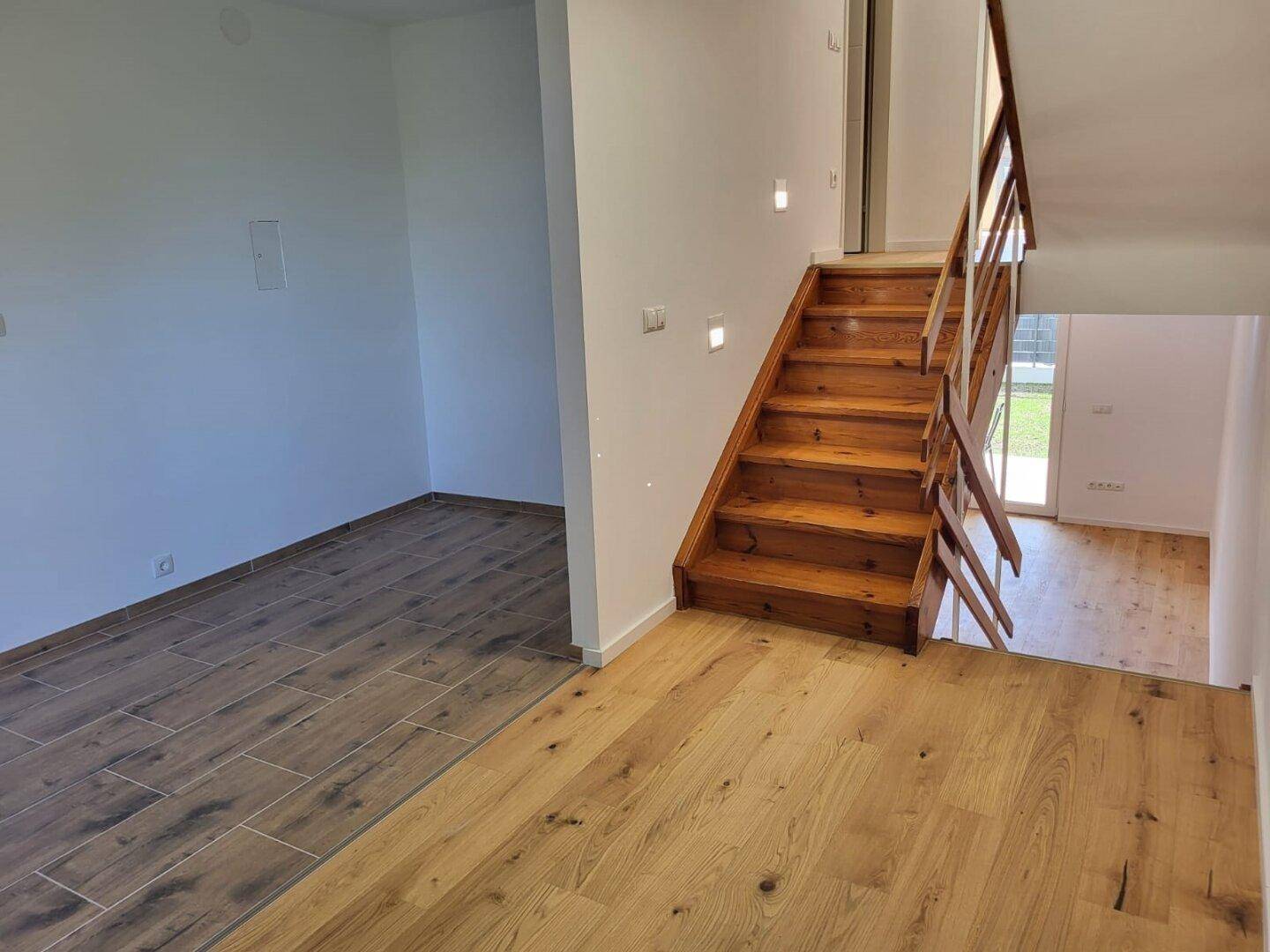 Übergangsbereich mit unterschiedlichen Bodenbelägen und einer Holztreppe, die die Etagen verbindet.