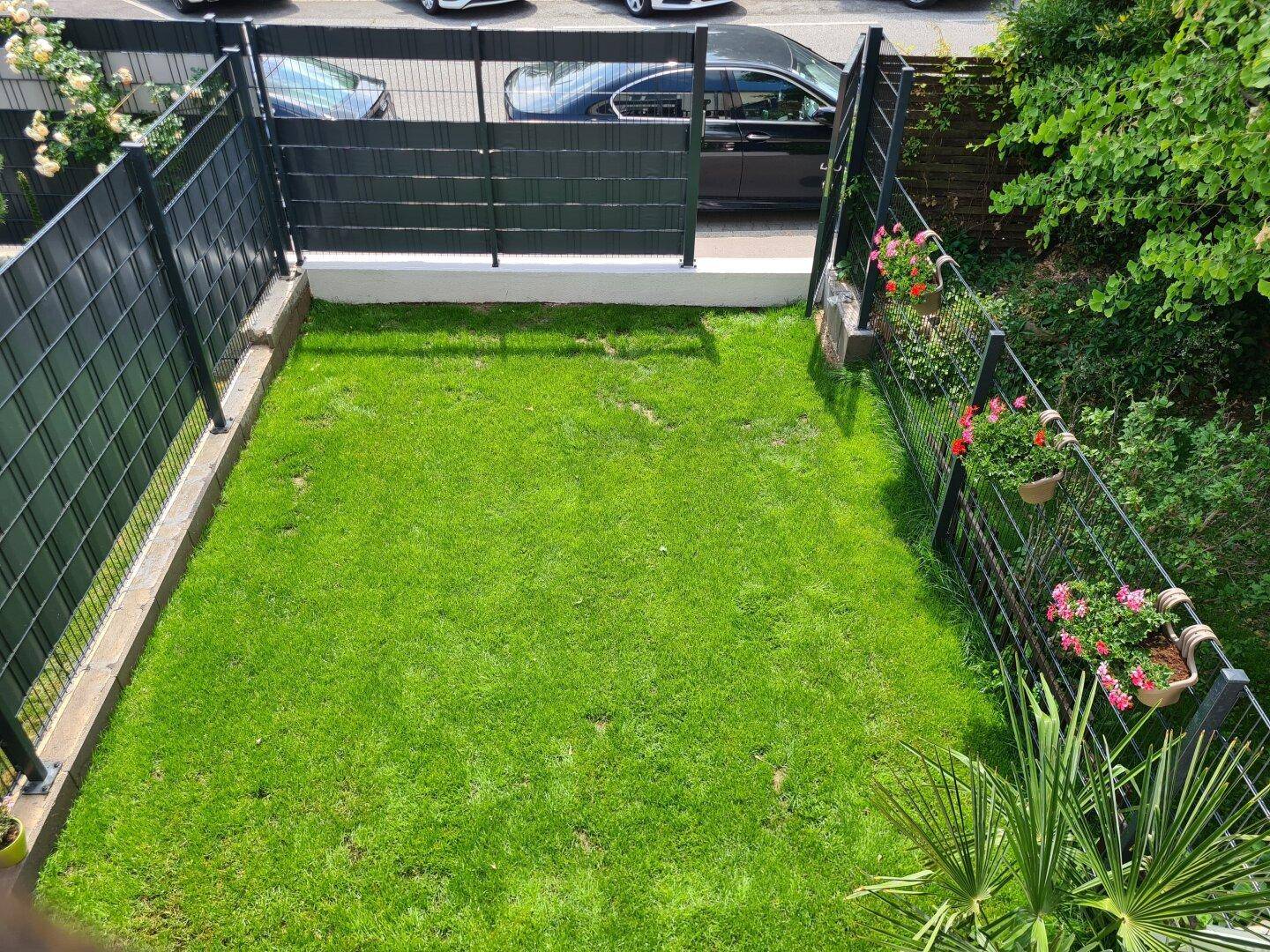 Gepflegter kleiner Gartenbereich mit Rasenfläche, umzäunt und mit Blick auf die Straße.