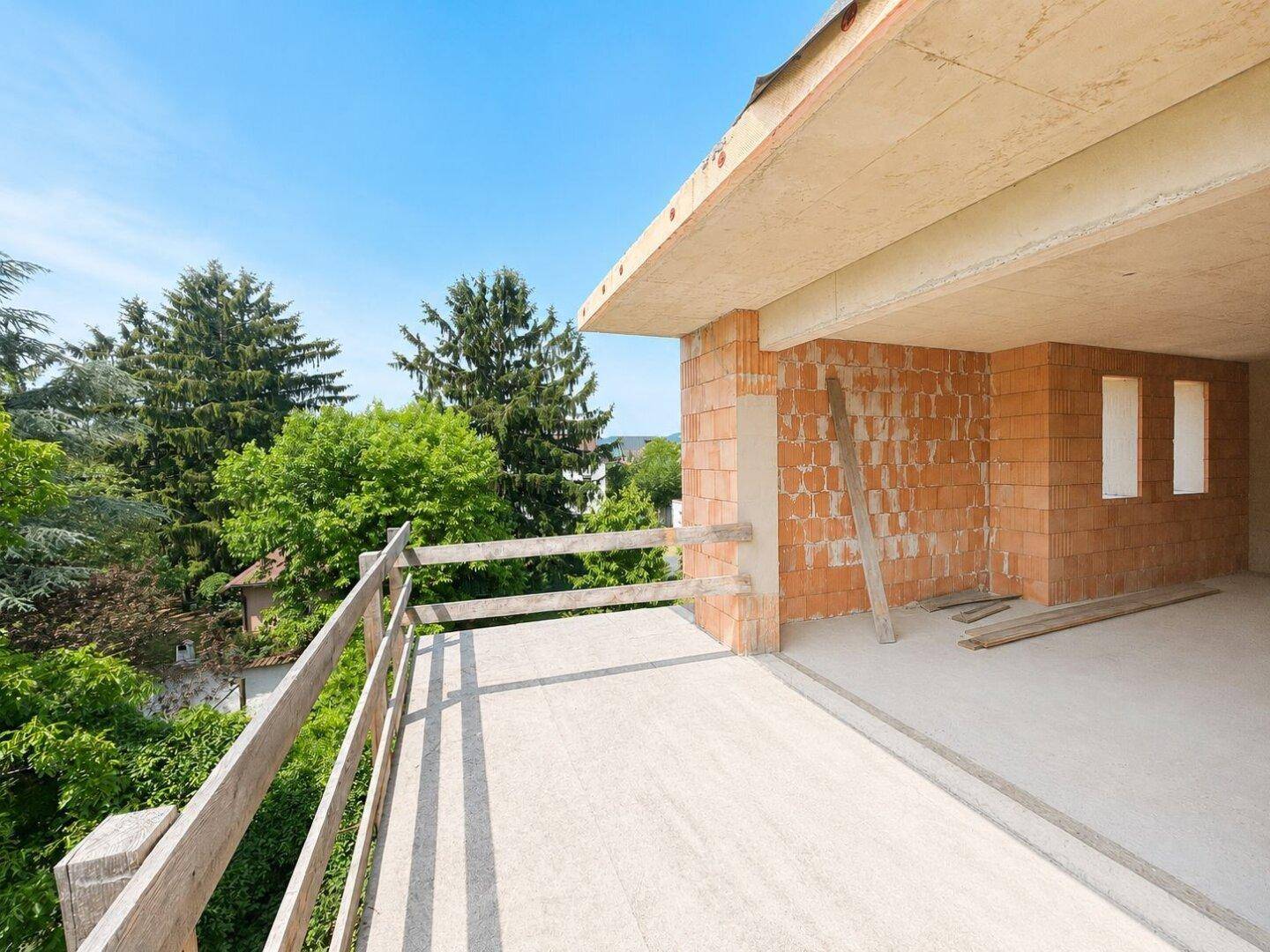 Unfertiger Balkon oder Terrasse im Rohbau mit Holzzaun und weitem Blick ins Grüne.