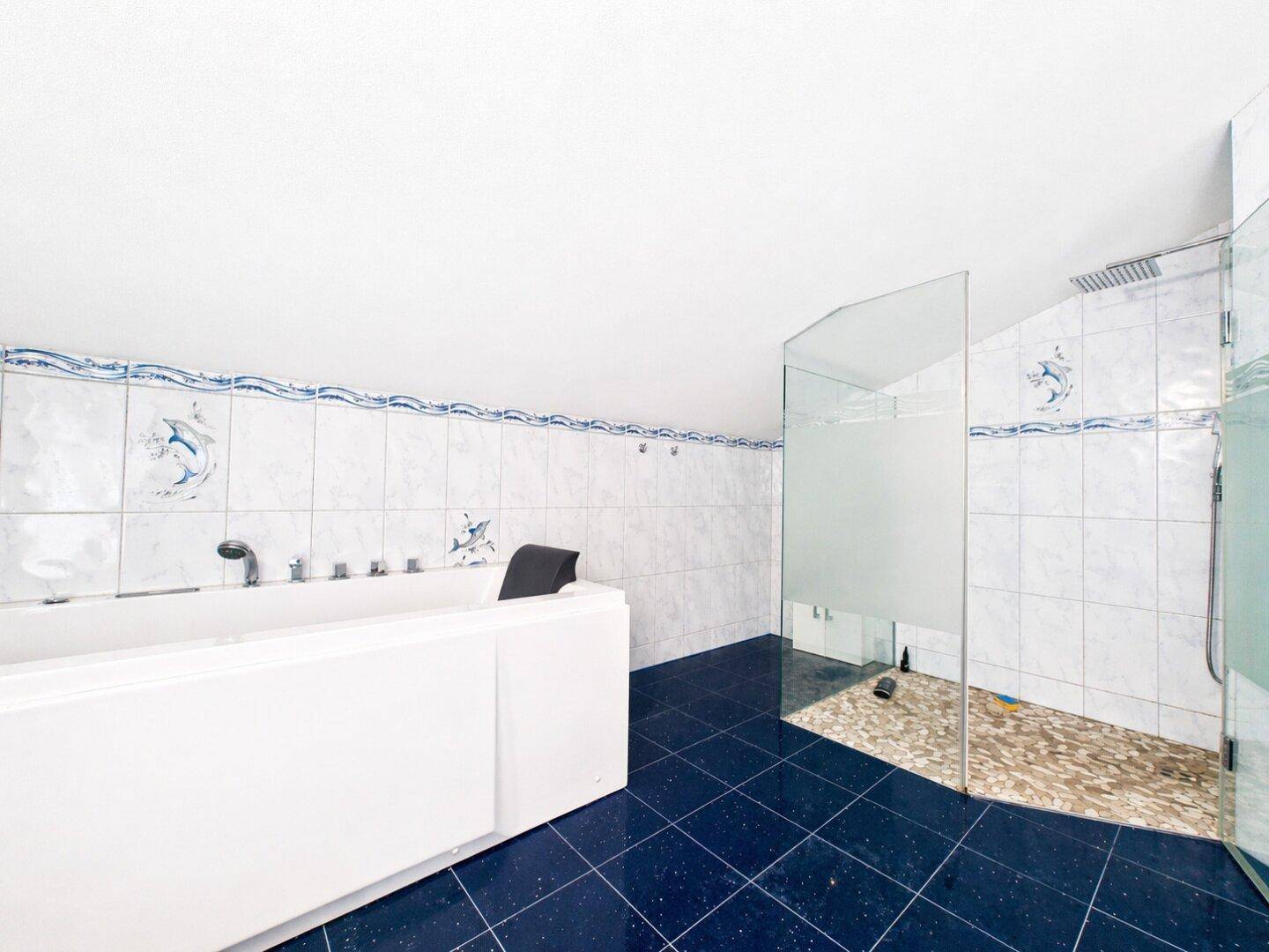 Geräumiges Badezimmer mit großer Badewanne, Duschbereich und blauen Bodenfliesen.