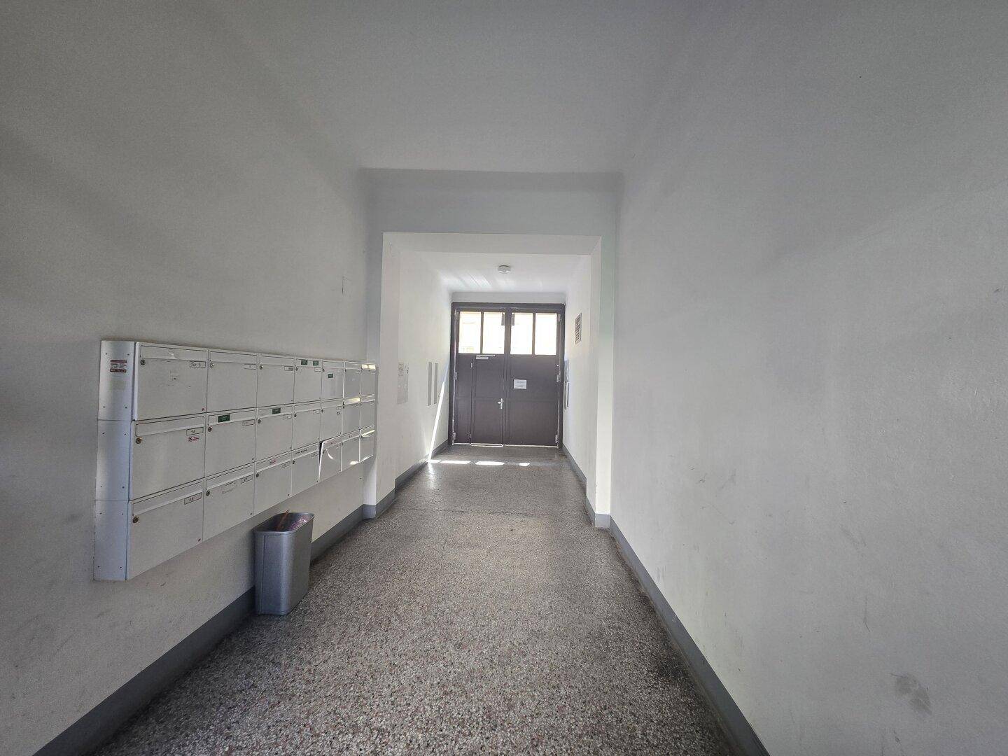 Heller Eingangsbereich eines Mehrfamilienhauses mit Briefkästen und Zugangstür.