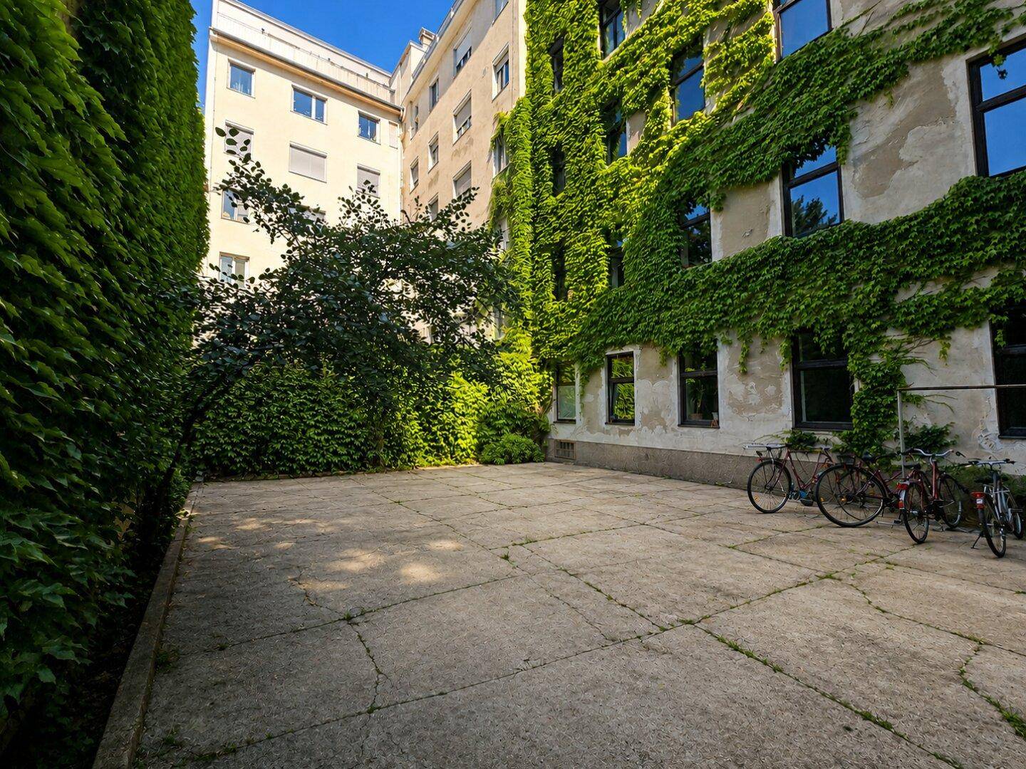 Innenhof mit viel Grün, bewachsenen Fassaden und Fahrradstellplätzen.