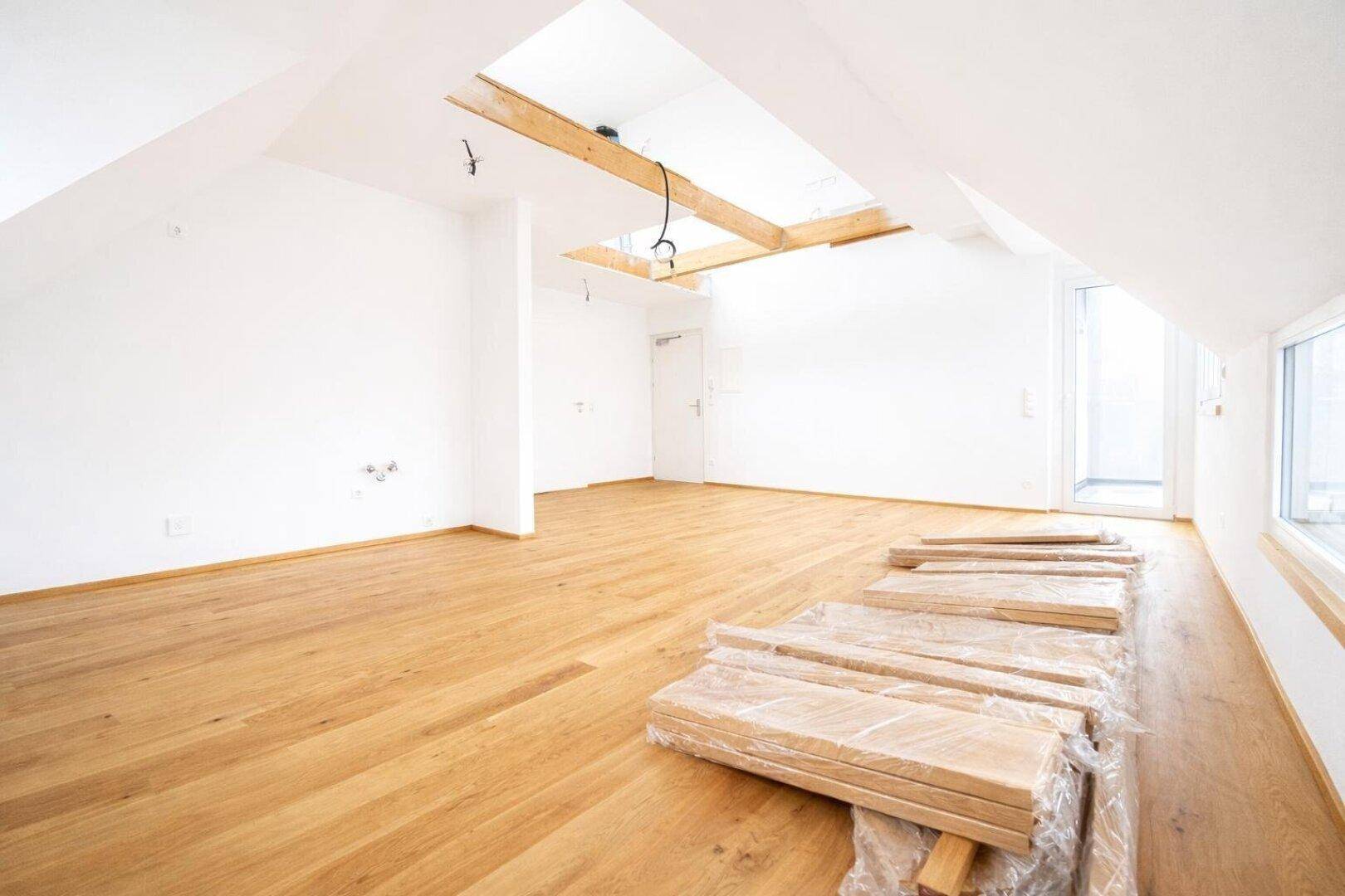 Heller Raum mit Holzboden, Dachfenster und vorbereiteten Baumaterialien in einem Neubau.