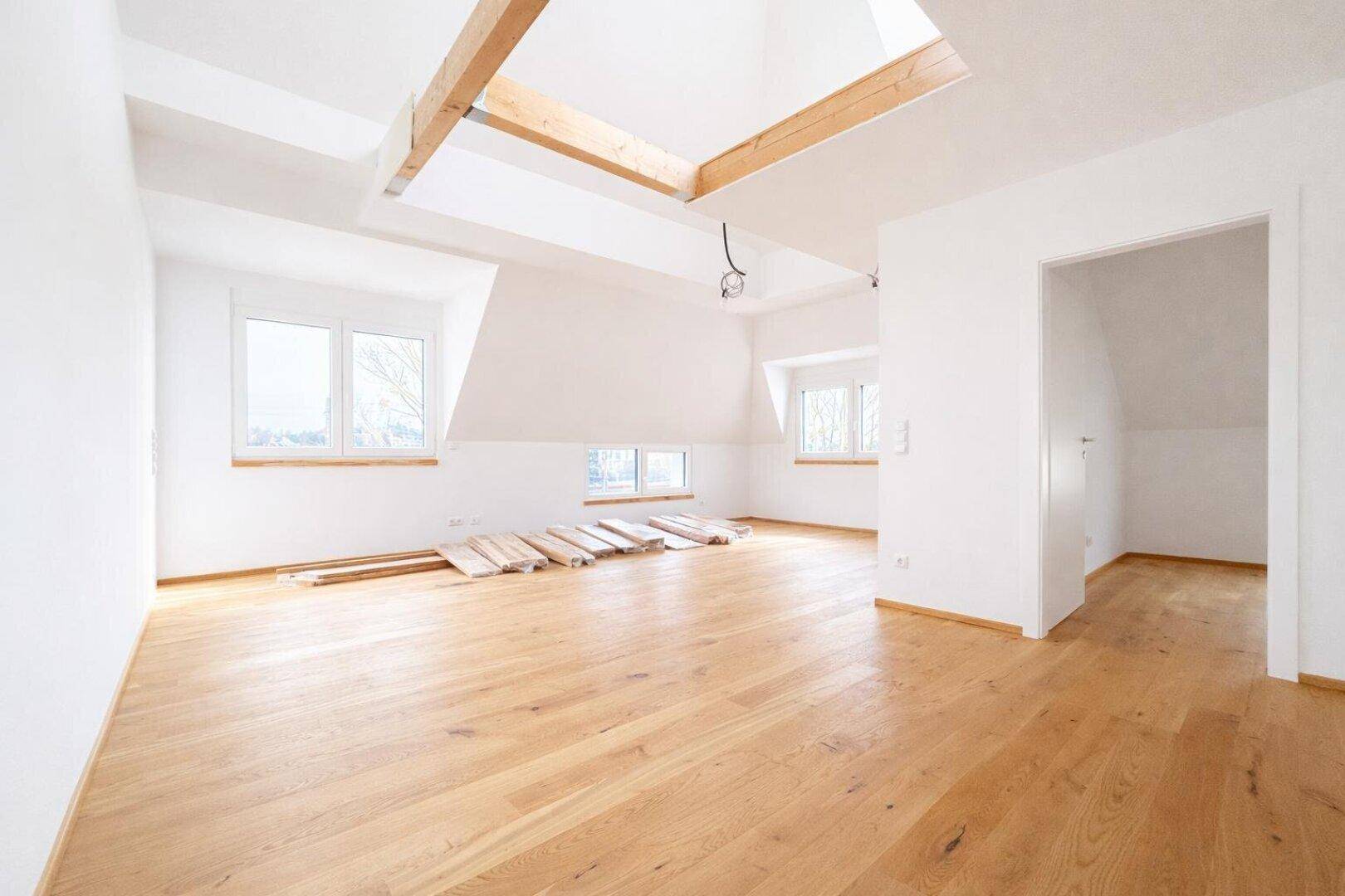 Geräumiger Wohnbereich mit Holzboden, Dachschrägen, sichtbaren Holzbalken und Dachfenstern.