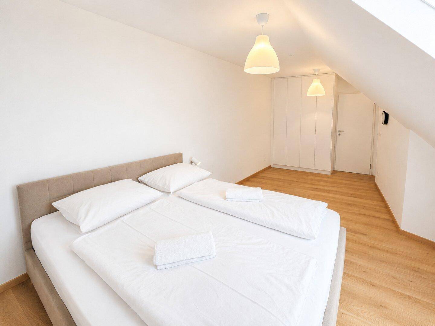 Gemütliches Schlafzimmer mit Doppelbett, Holzfußboden und Dachschräge, hell und einladend.