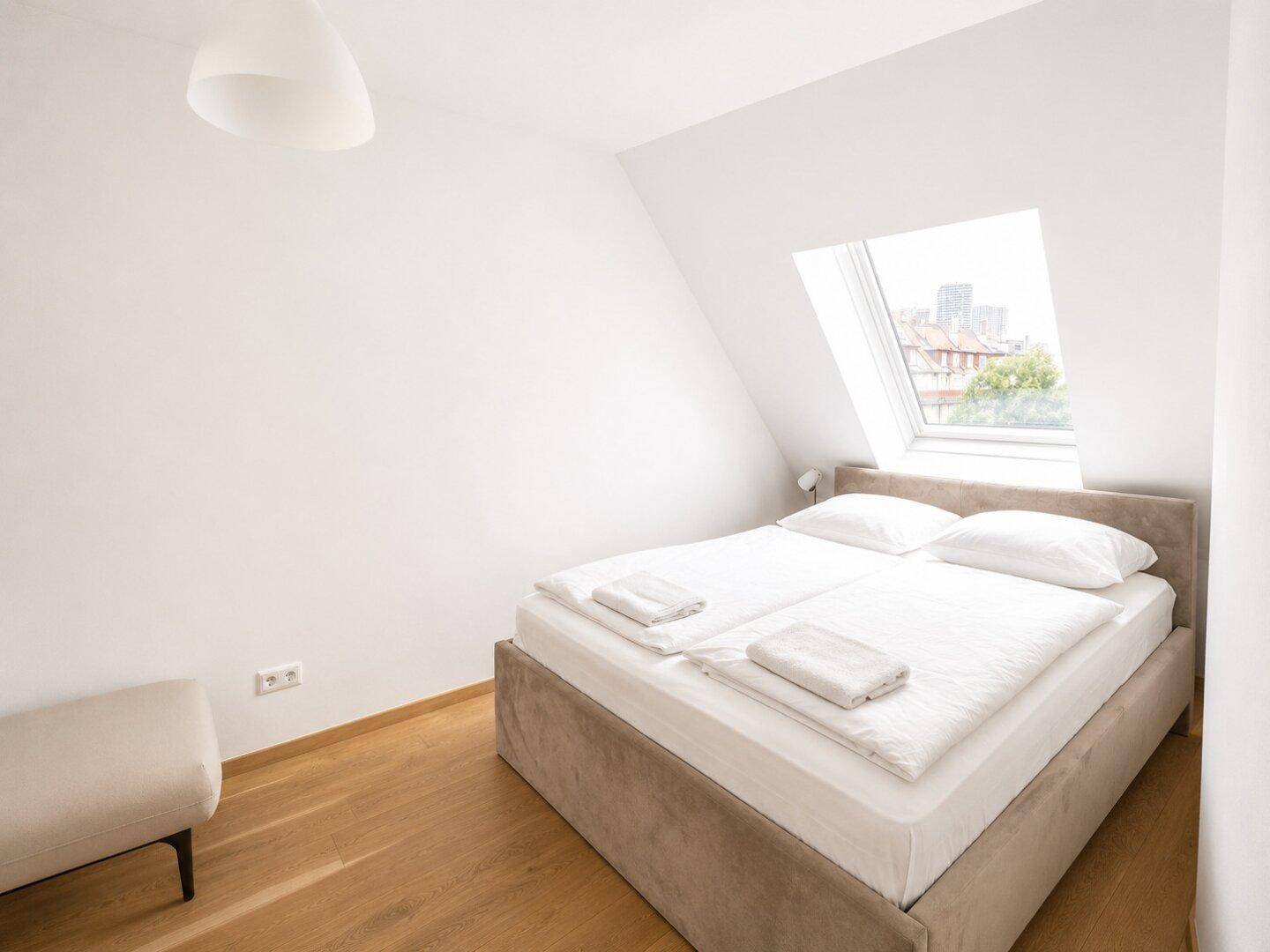 Helles Schlafzimmer mit Doppelbett, Holzfußboden und Dachfenster, das viel Tageslicht spendet.