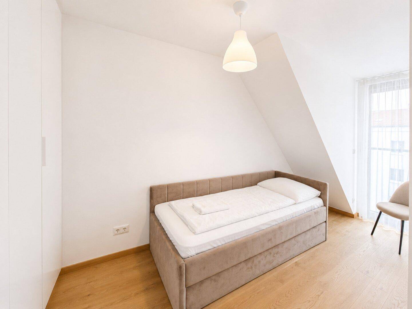 Helles Schlafzimmer mit Einzelbett, Holzfußboden und Dachschräge, ideal als Gästezimmer.