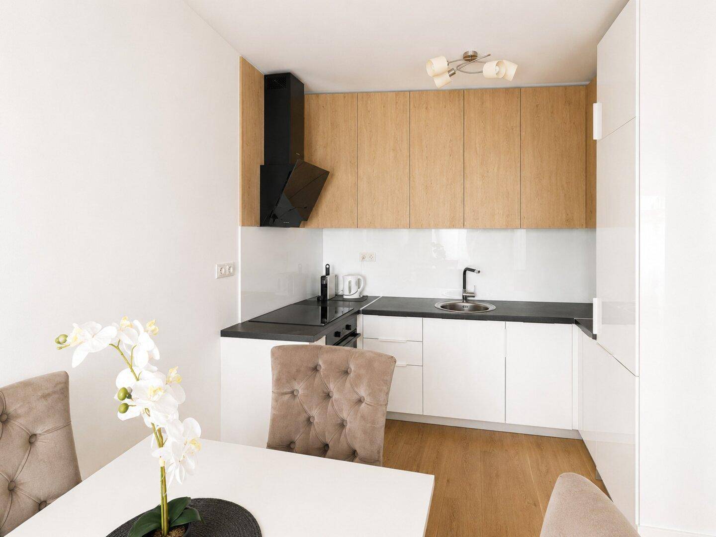 Moderne Küche mit weißen und holzfarbenen Schränken, schwarzer Arbeitsplatte und Essbereich.