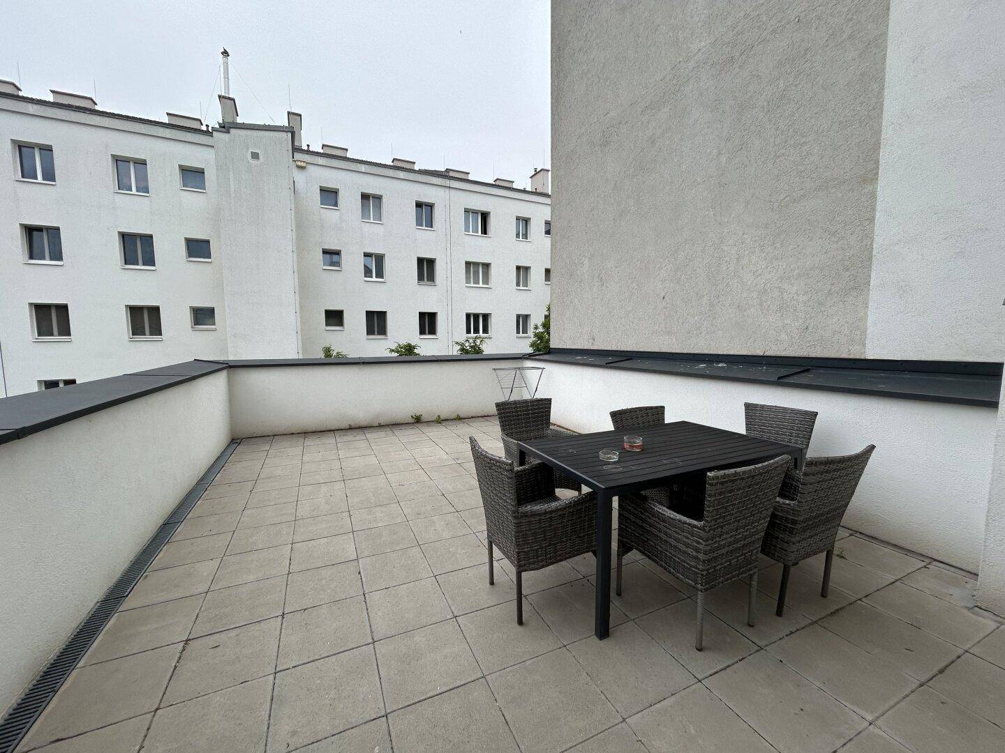 Geräumige Außenterrasse mit Gartenmöbeln, umgeben von Gebäuden, ideal zum Entspannen.