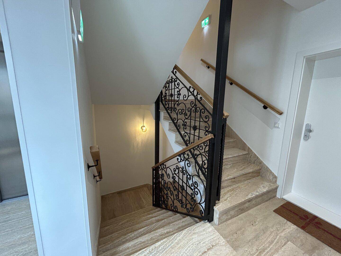 Elegantes Treppenhaus mit schmiedeeisernem Geländer und Natursteinboden in einem modernen Gebäude.