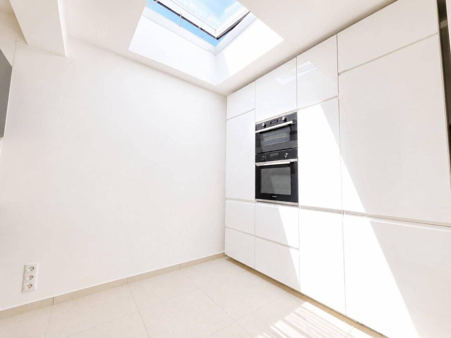 Heller Küchenbereich mit weißen Einbauschränken, Backofen, Mikrowelle und einem Dachfenster.