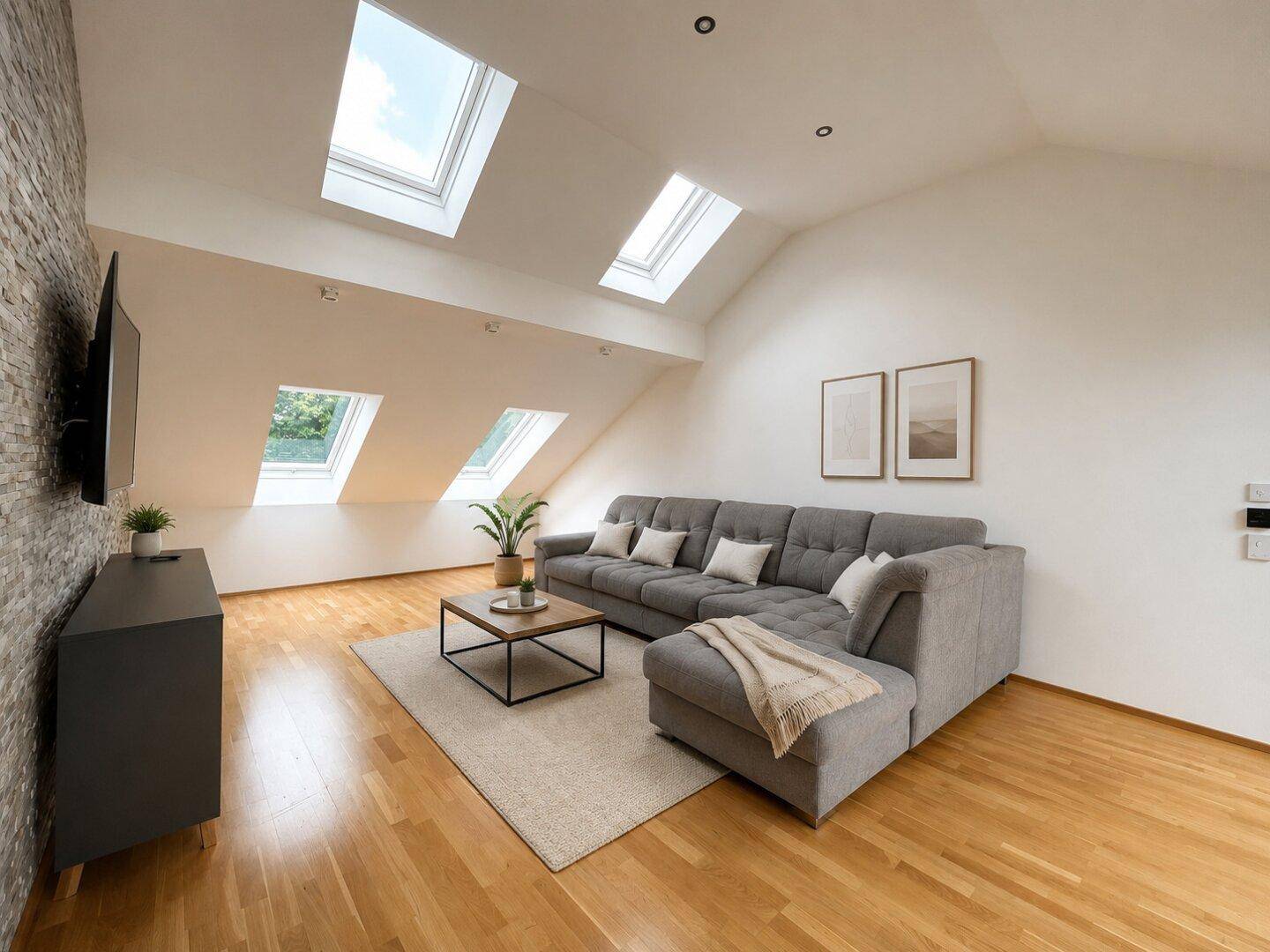 Helles Wohnzimmer im Dachgeschoss mit schrägen Wänden, Dachfenstern und modernem Sofa.