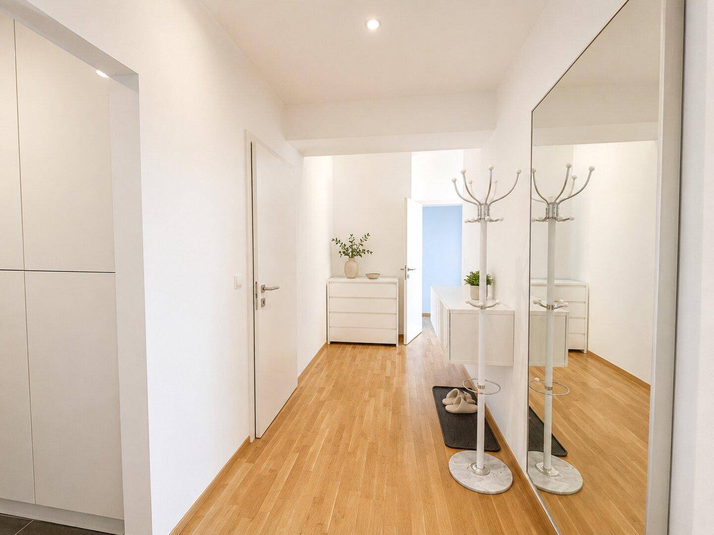 Heller Flur mit Holzboden, großem Spiegel und weißem Einbauschrank.