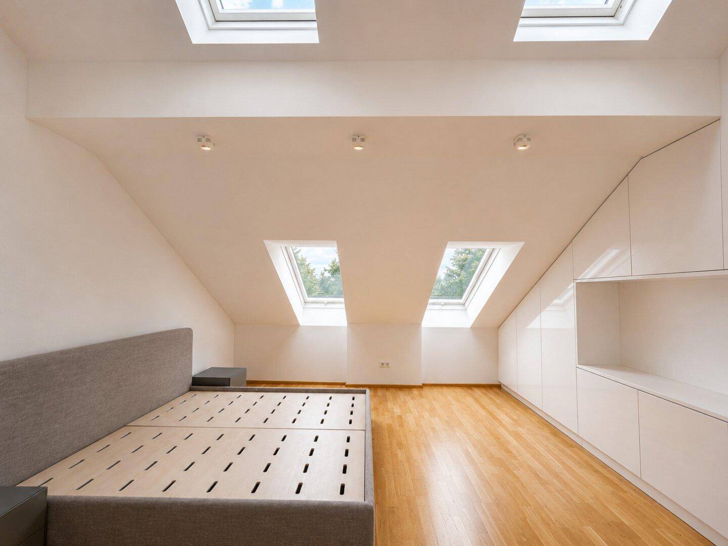 Schlafzimmer im Dachgeschoss mit schrägen Wänden, Dachfenstern und integrierten Schränken.