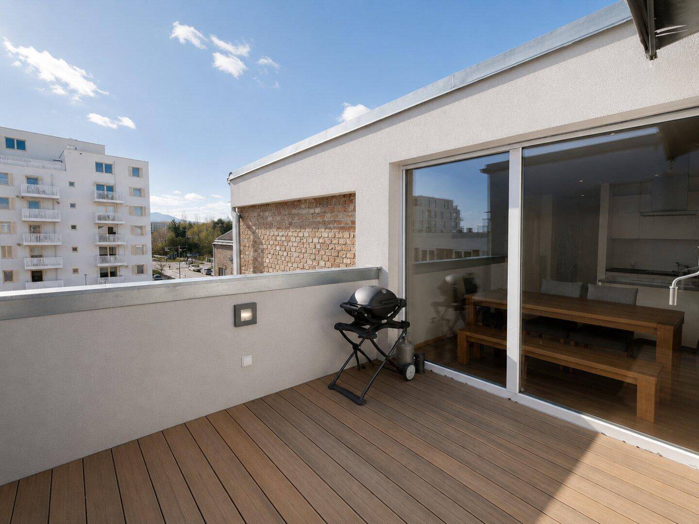 Geräumige Terrasse mit Holzboden, Grill und Blick auf die Umgebung.