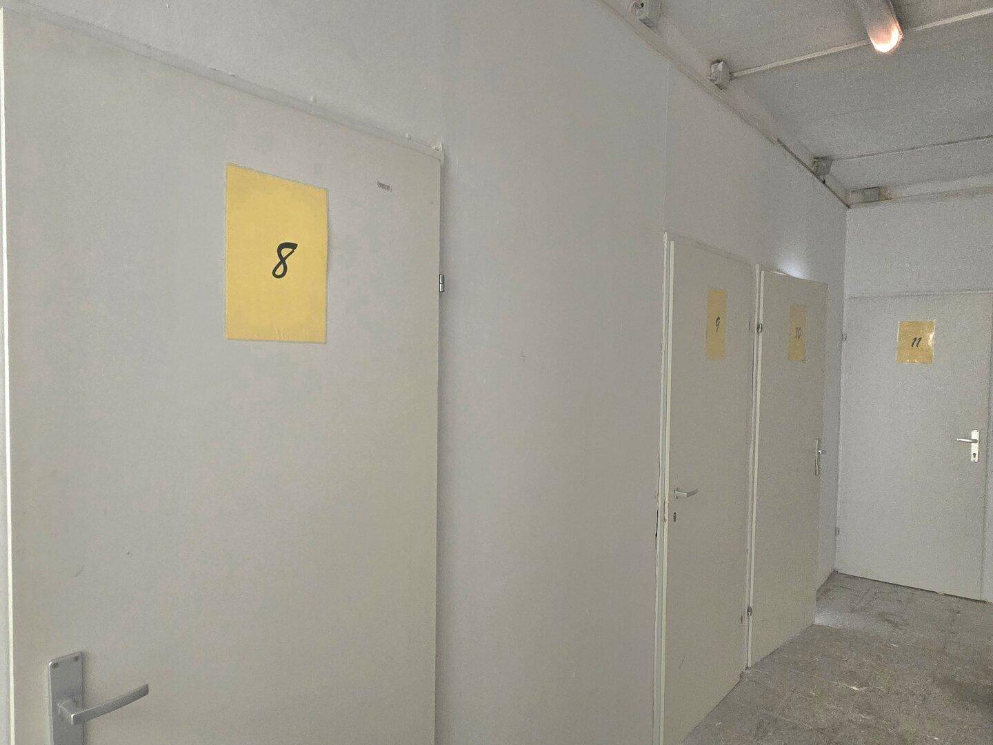 Langer Flur mit mehreren Türen, jeweils mit gelben Nummern gekennzeichnet, in einem Gemeinschaftsbereich.