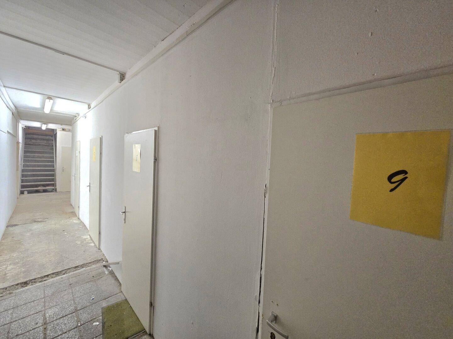 Heller Flur mit mehreren Türen und einem Treppenaufgang im Hintergrund, gut beleuchtet.