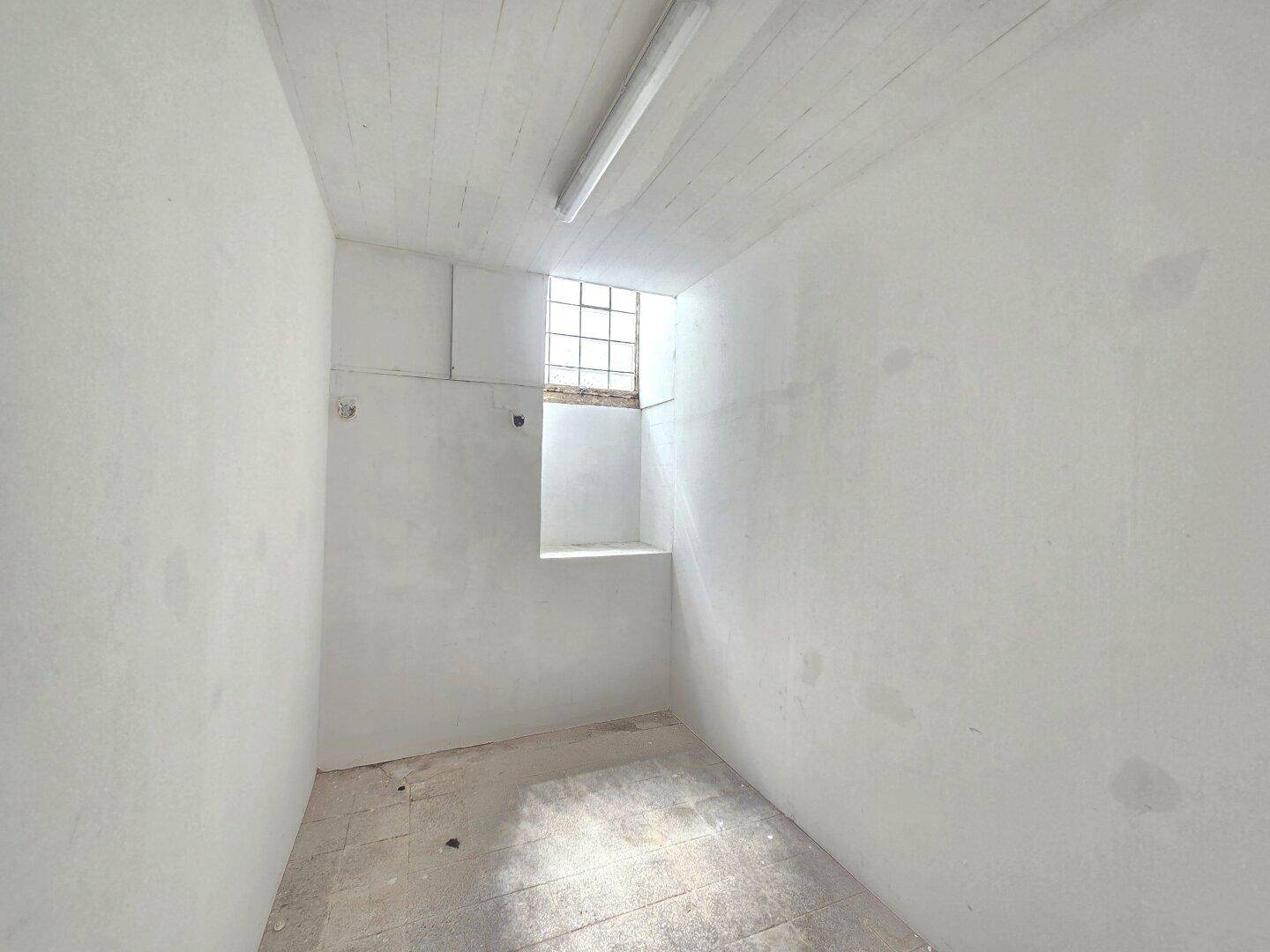 Leerer Abstellraum mit weißen Wänden, kleinem Fenster und Deckenbeleuchtung, ideal für Lagerung.
