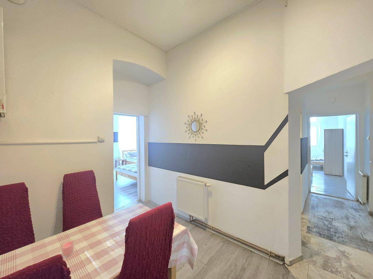 Essbereich mit rotem Stuhlbezug und Wanddekoration, angrenzend an ein Schlafzimmer.