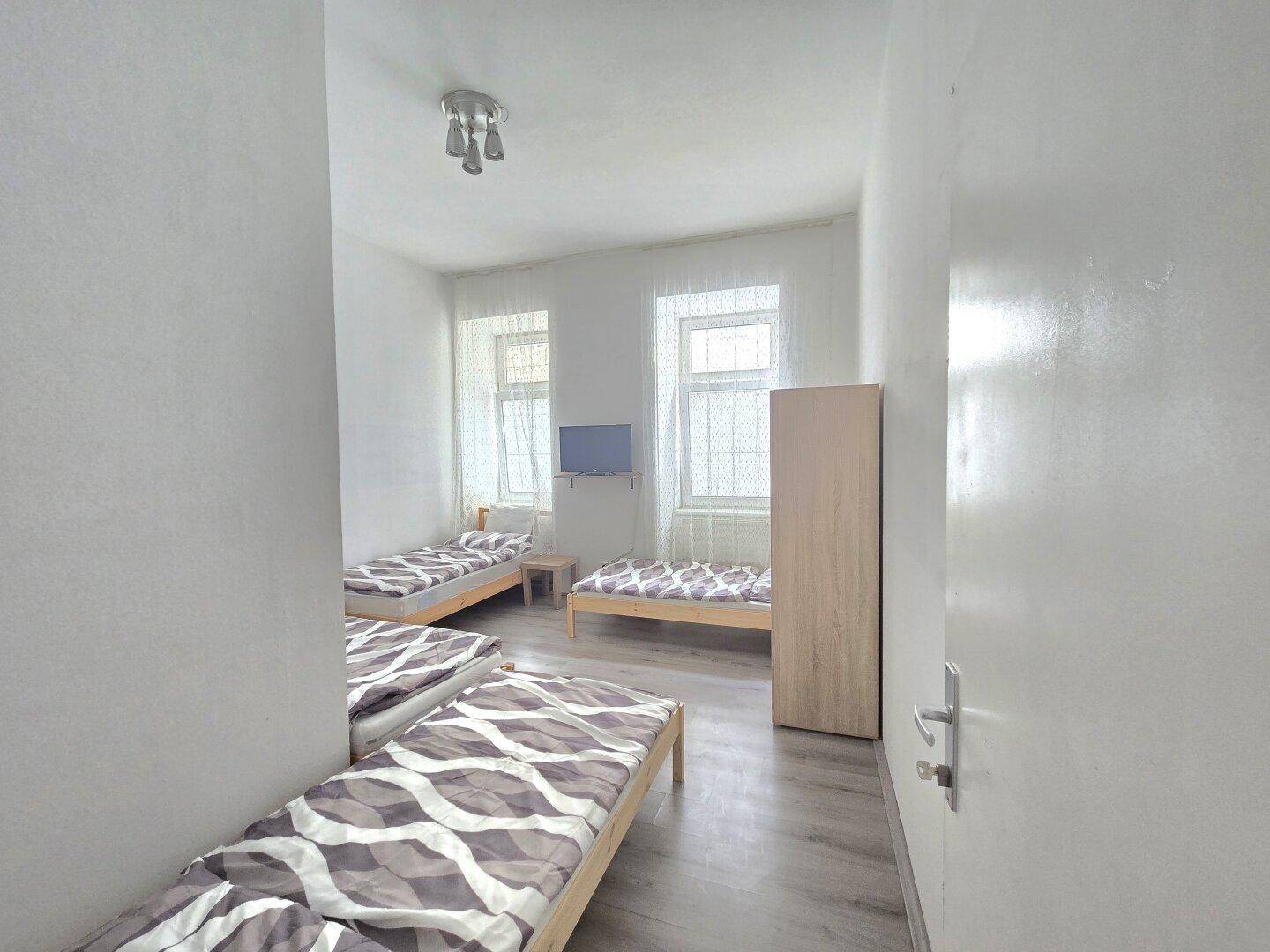 Geräumiges Schlafzimmer mit drei Einzelbetten und hellen Fenstern, bietet Platz für mehrere Personen.