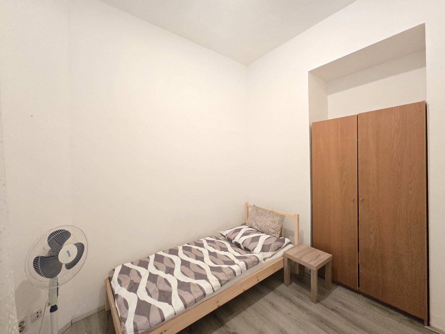 Einzelnes Schlafzimmer mit Bett, Nachttisch und Kleiderschrank, bietet eine einfache Unterkunft.