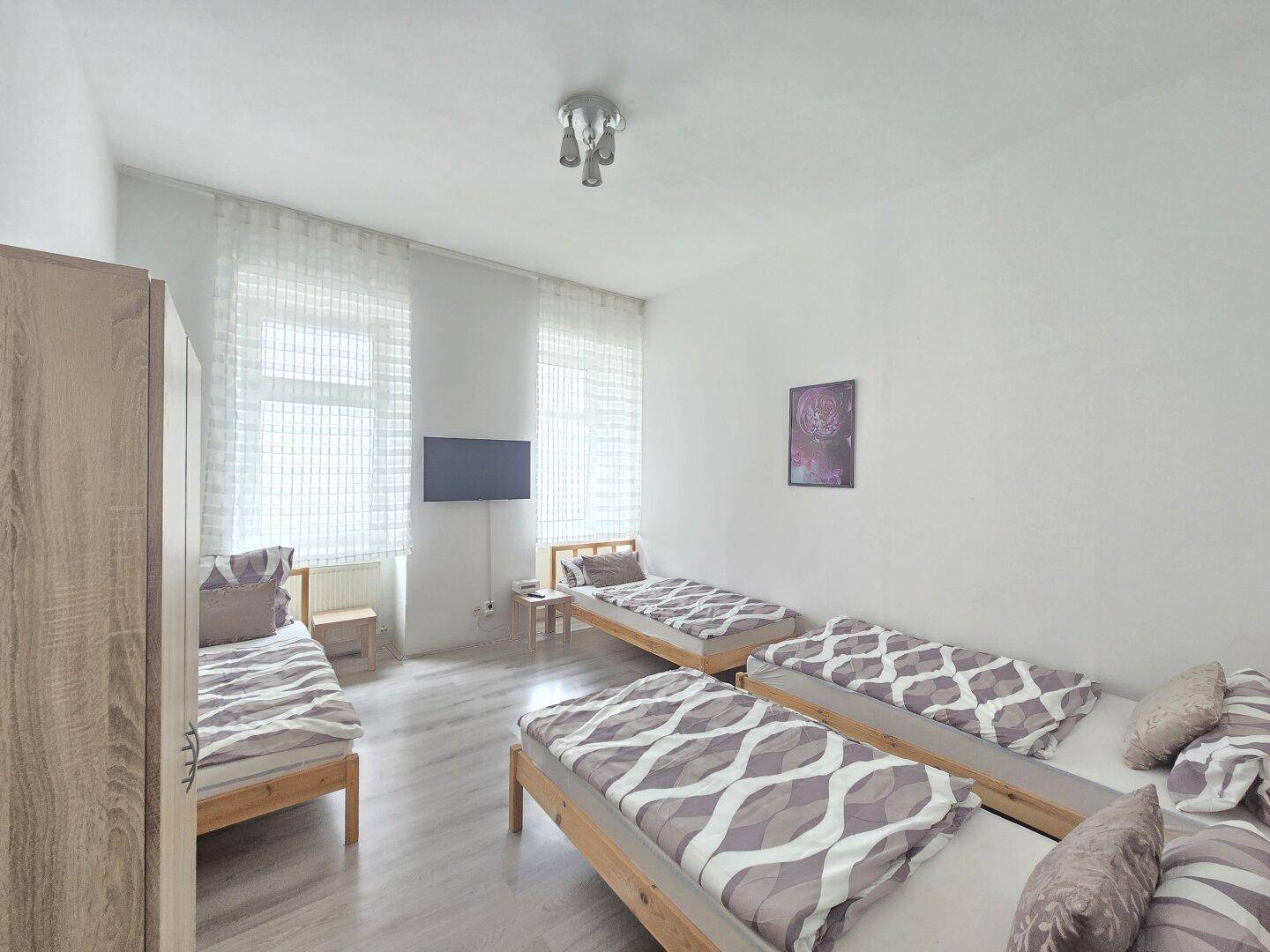 Großes Schlafzimmer mit mehreren Einzelbetten, Kleiderschrank und hellen Fenstern.