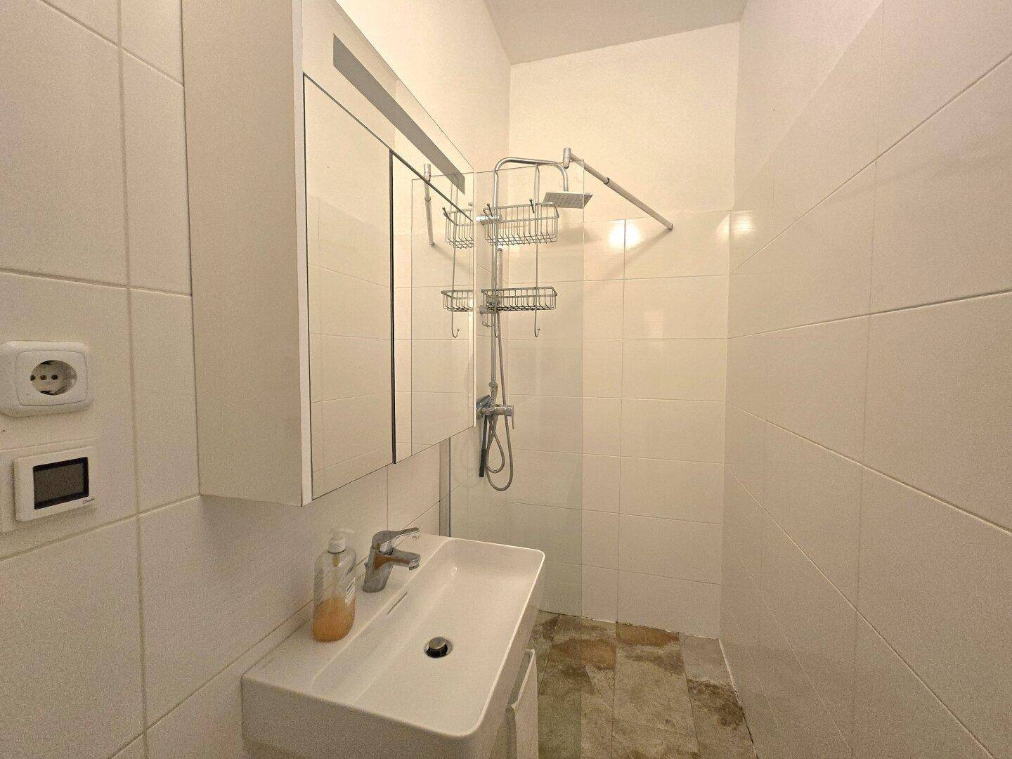 Modernes Badezimmer mit Waschbecken, Spiegelschrank und Duschbereich, komplett gefliest.
