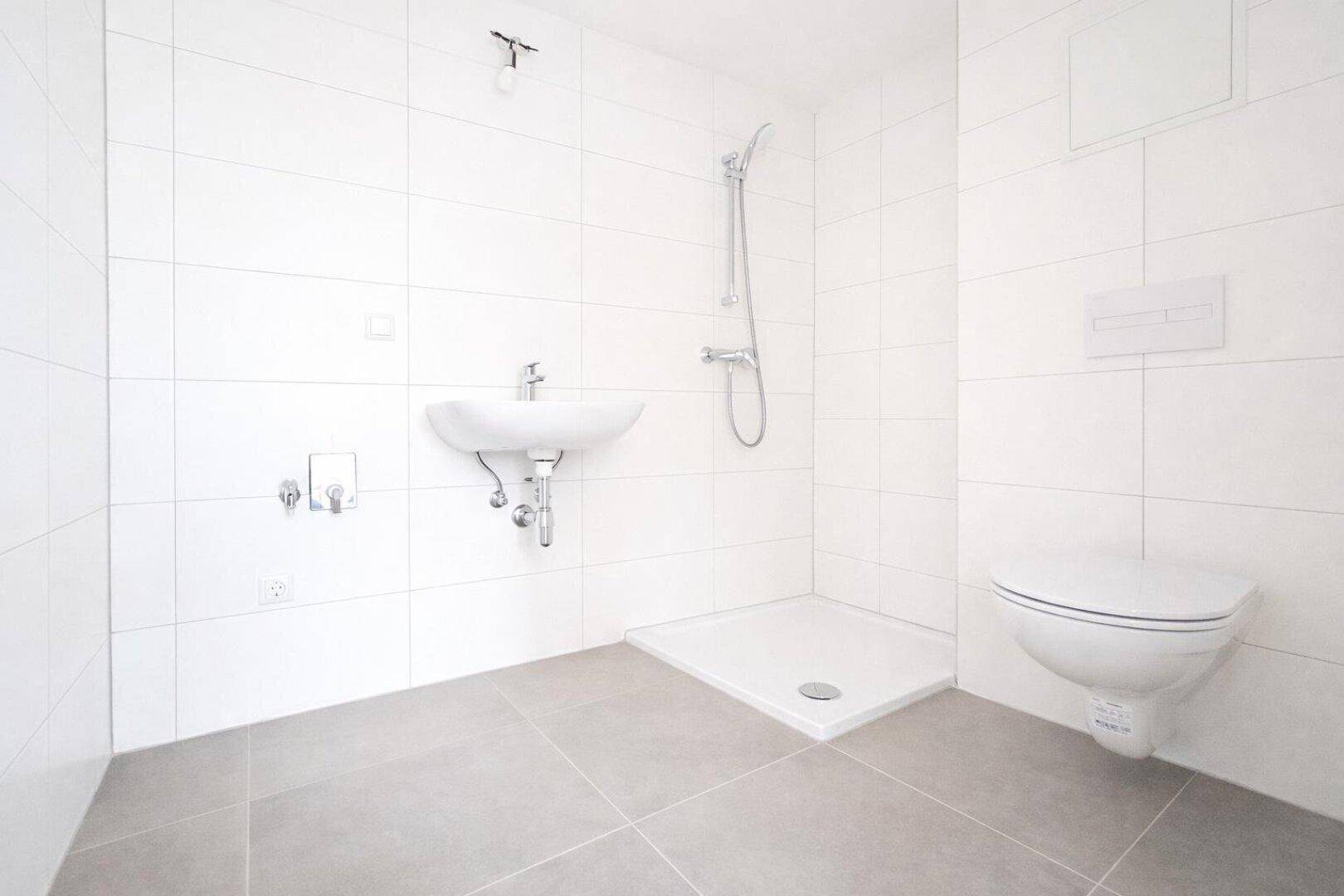 Modernes Badezimmer mit weißen Fliesen, ebenerdiger Dusche, Waschbecken und wandhängendem WC.