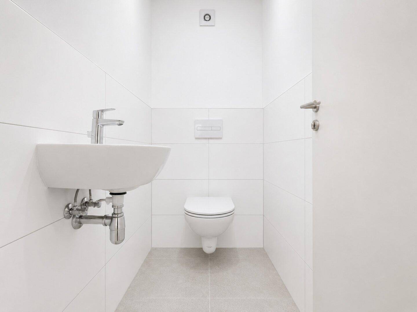Kleines Gäste-WC mit weißen Fliesen, wandhängendem WC und modernem Waschbecken.