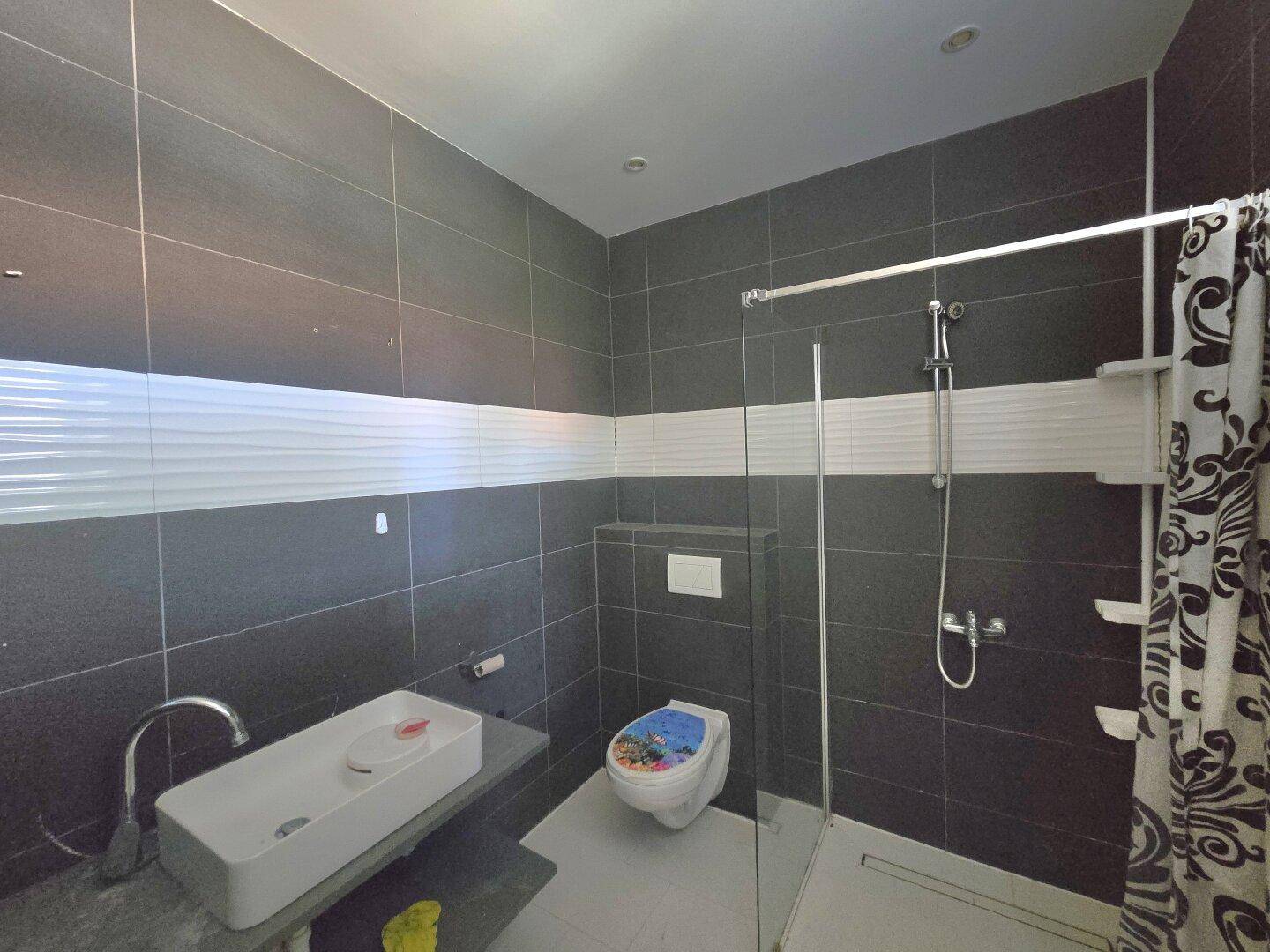 Modernes Badezimmer mit dunklen Fliesen, einer ebenerdigen Dusche und einem stilvollen Waschbecken.