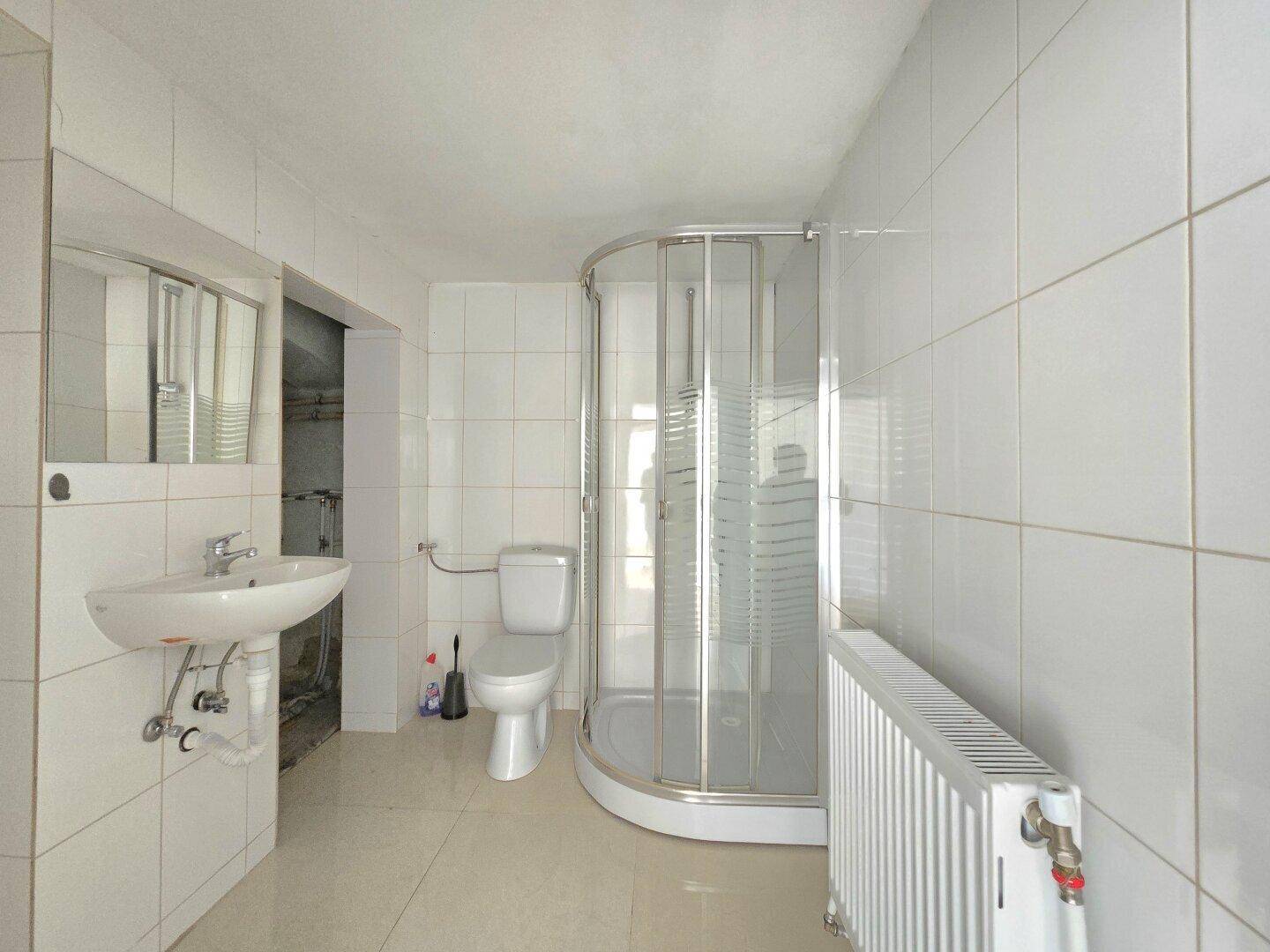 Badezimmer mit weißen Fliesen, Duschkabine, WC, Waschbecken und Heizkörper für angenehme Wärme.