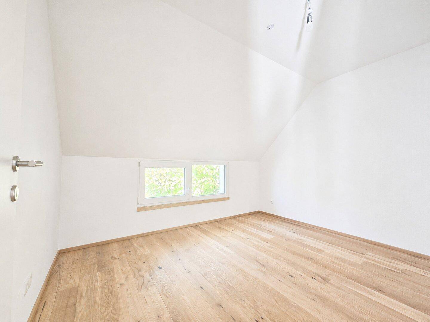 Helles Schlafzimmer im Dachgeschoss mit schrägen Wänden, Holzboden und Fenster.