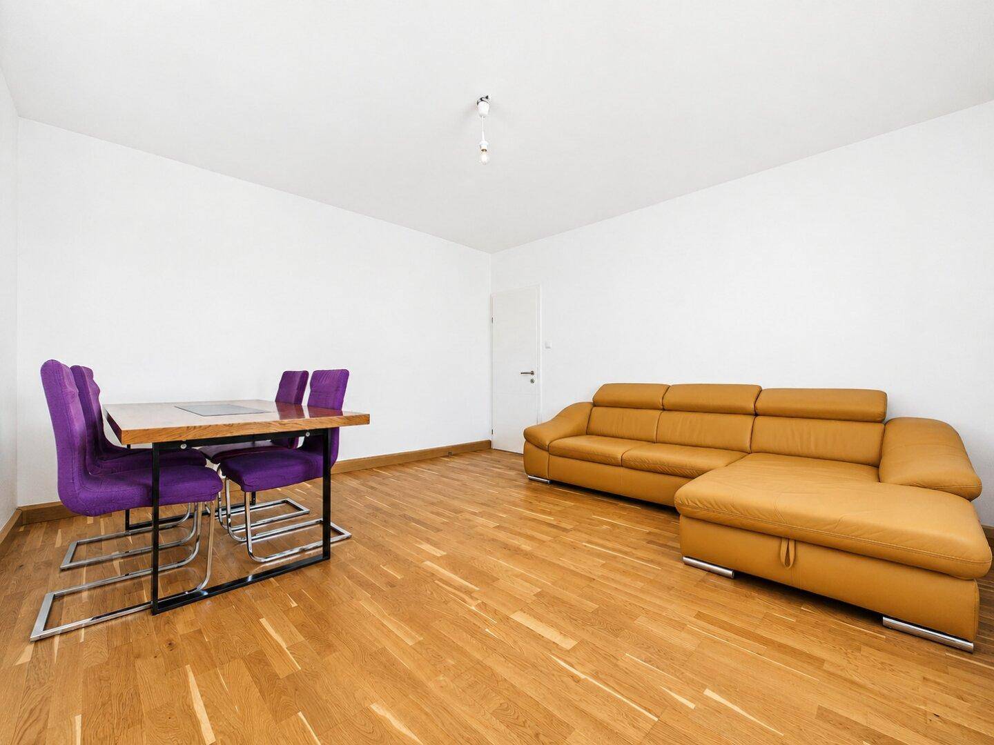 Heller Wohn- und Essbereich mit bequemer Couch, Esstisch und Parkettboden.