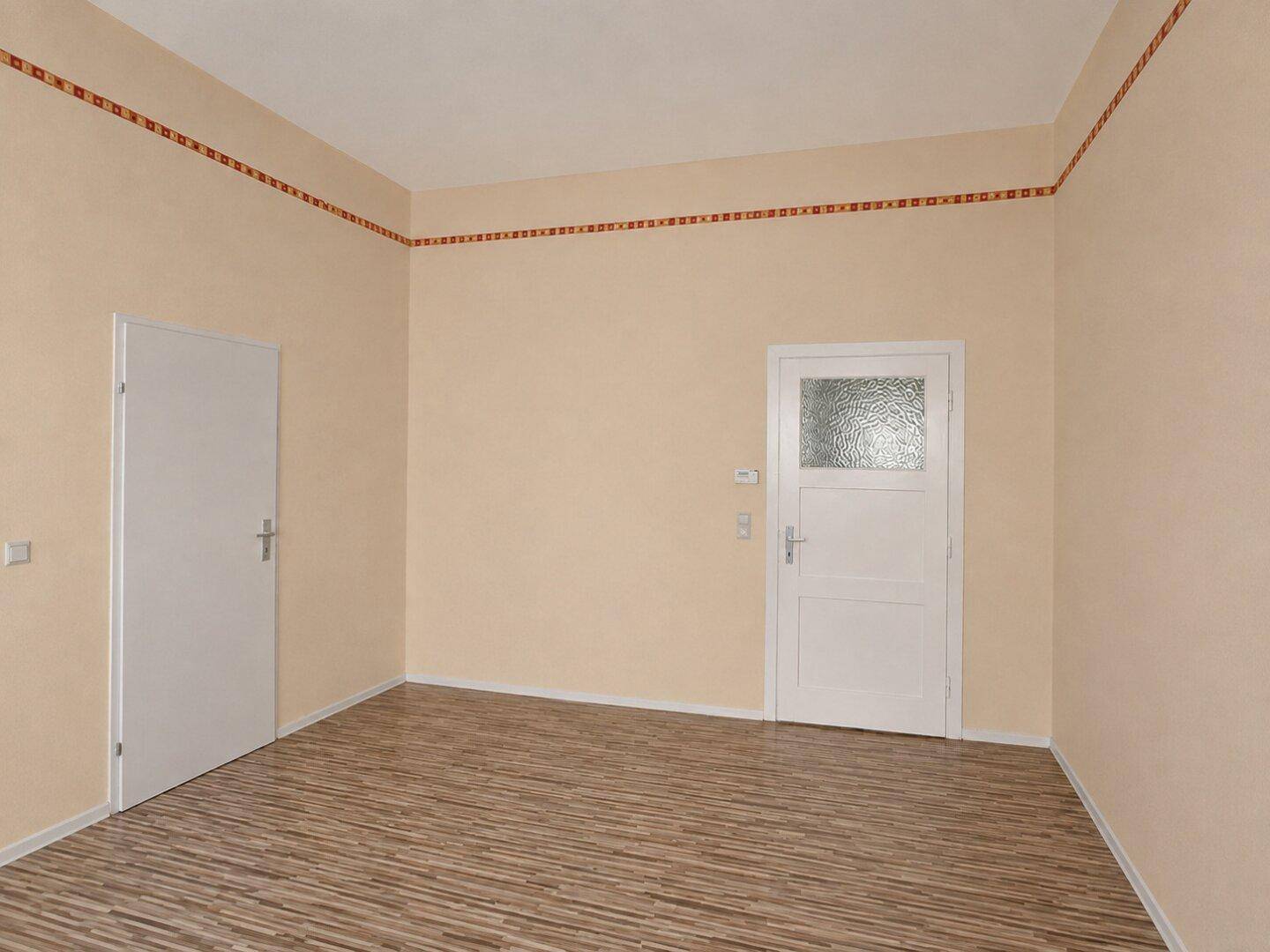 Leerer Raum mit beigen Wänden, Laminatboden und zwei Türen, eine davon mit Glaseinsatz.