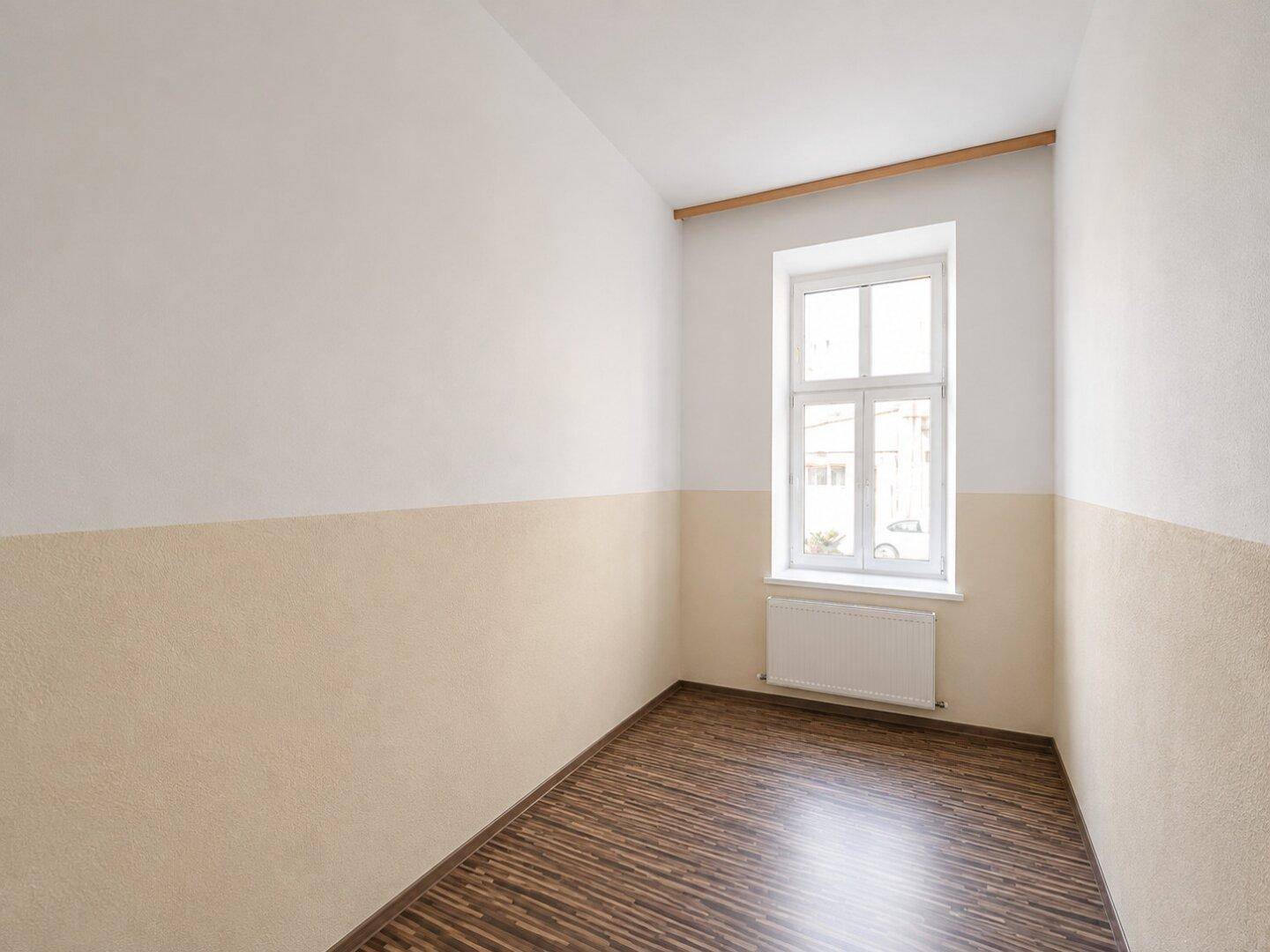 Kleiner Raum mit zweifarbigen Wänden, Laminatboden, einem Fenster und Heizkörper.