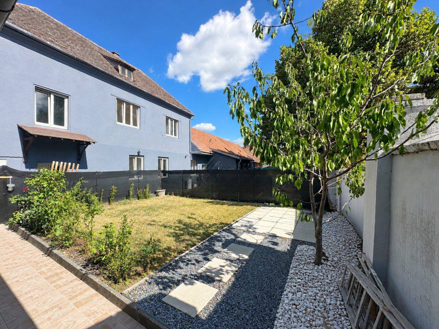 Gepflegter Gartenbereich hinter dem Haus mit Rasenfläche, Kiesweg und einem jungen Baum.