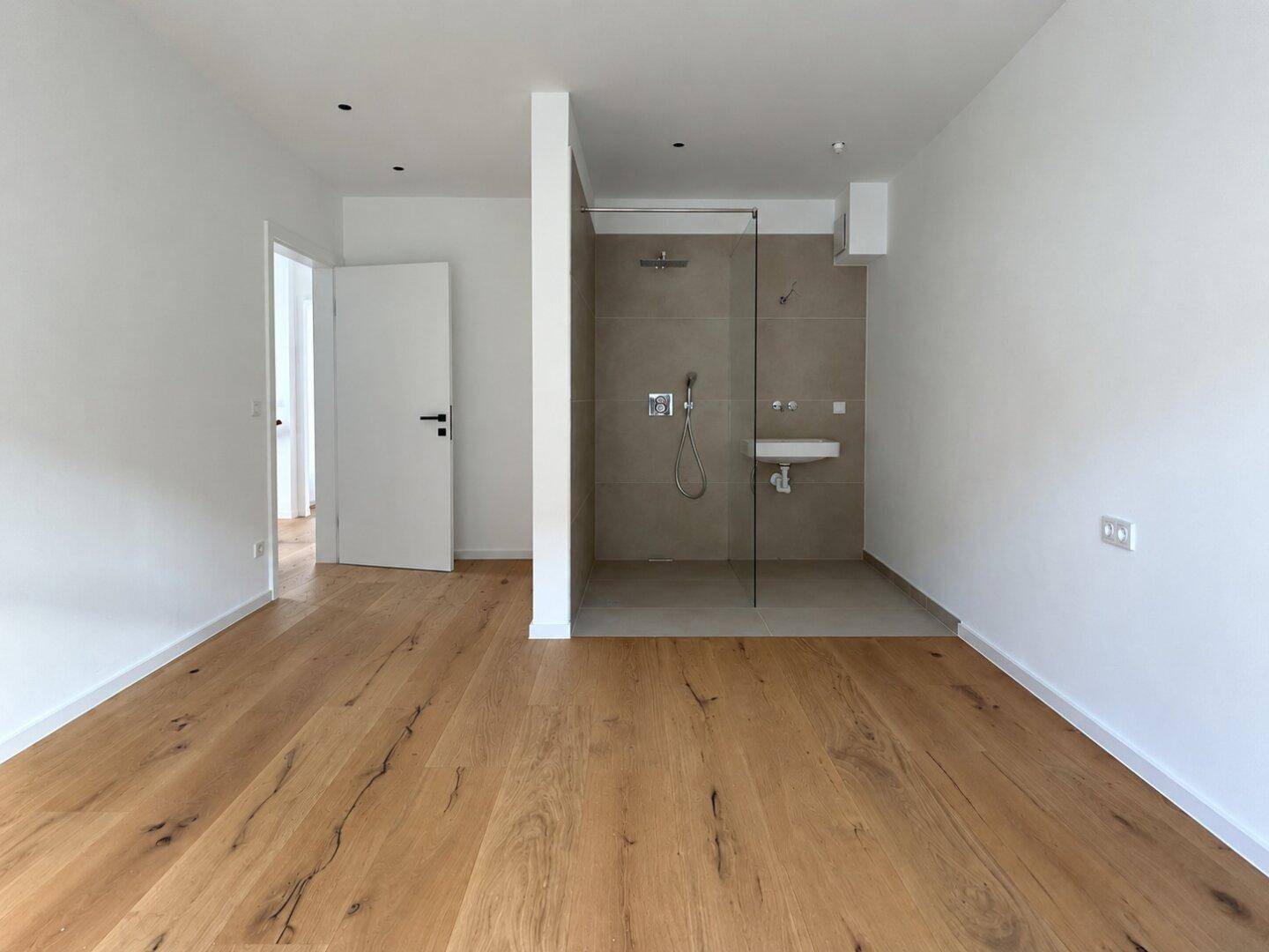 Helles Schlafzimmer mit Eichenparkett und offenem Duschbereich mit modernem Waschbecken.