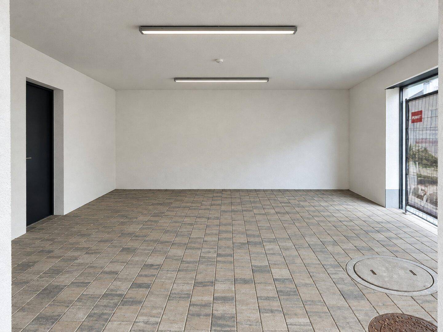 Geräumige Garage oder Parkfläche mit Fliesenboden und Zugang zum Außenbereich.